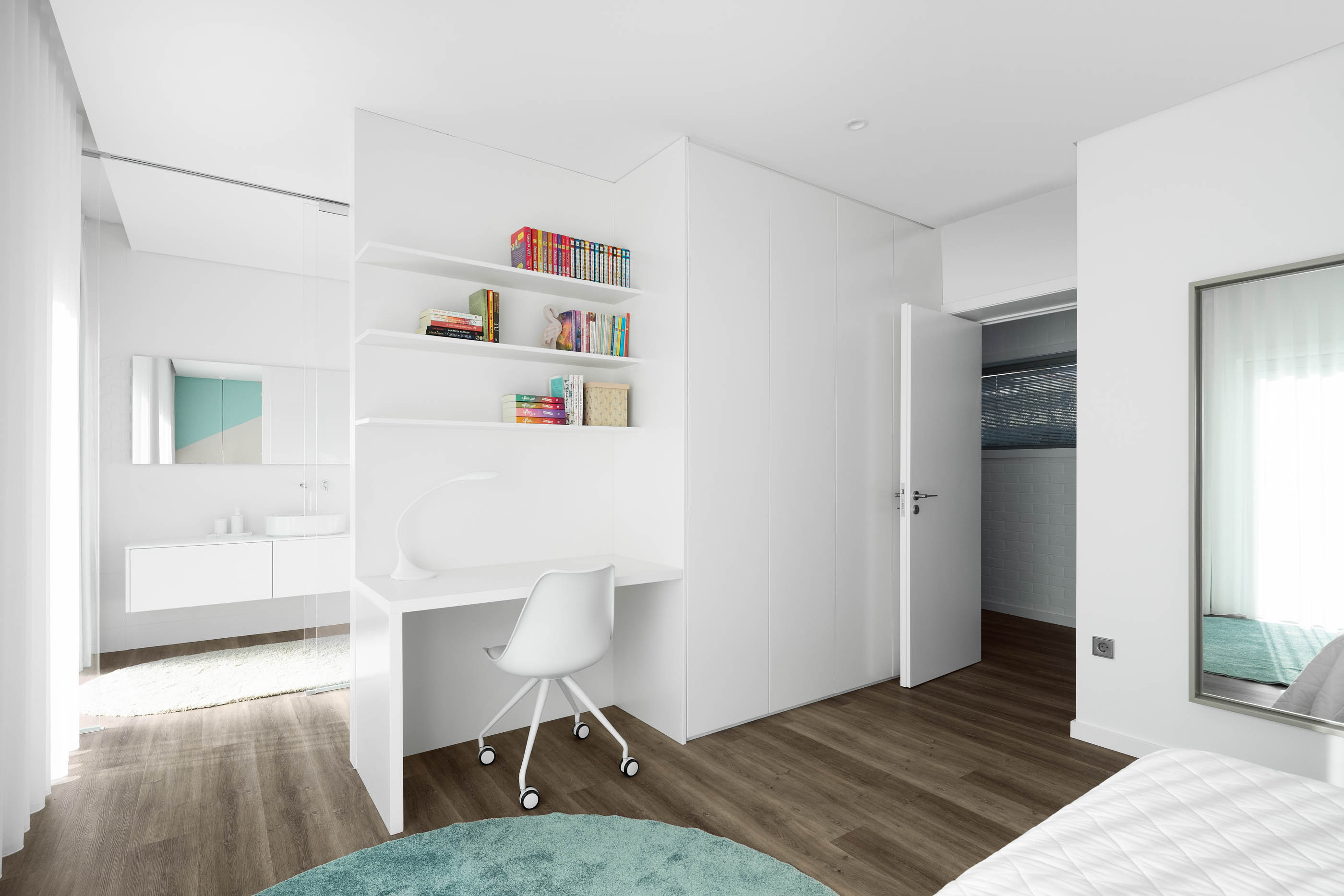 Quarto com secretária branca, estantes, cama e casa de banho em tons de branco e azul, pavimento em madeira. — Reabilitação Casa J arquitetura Frari em Portugal