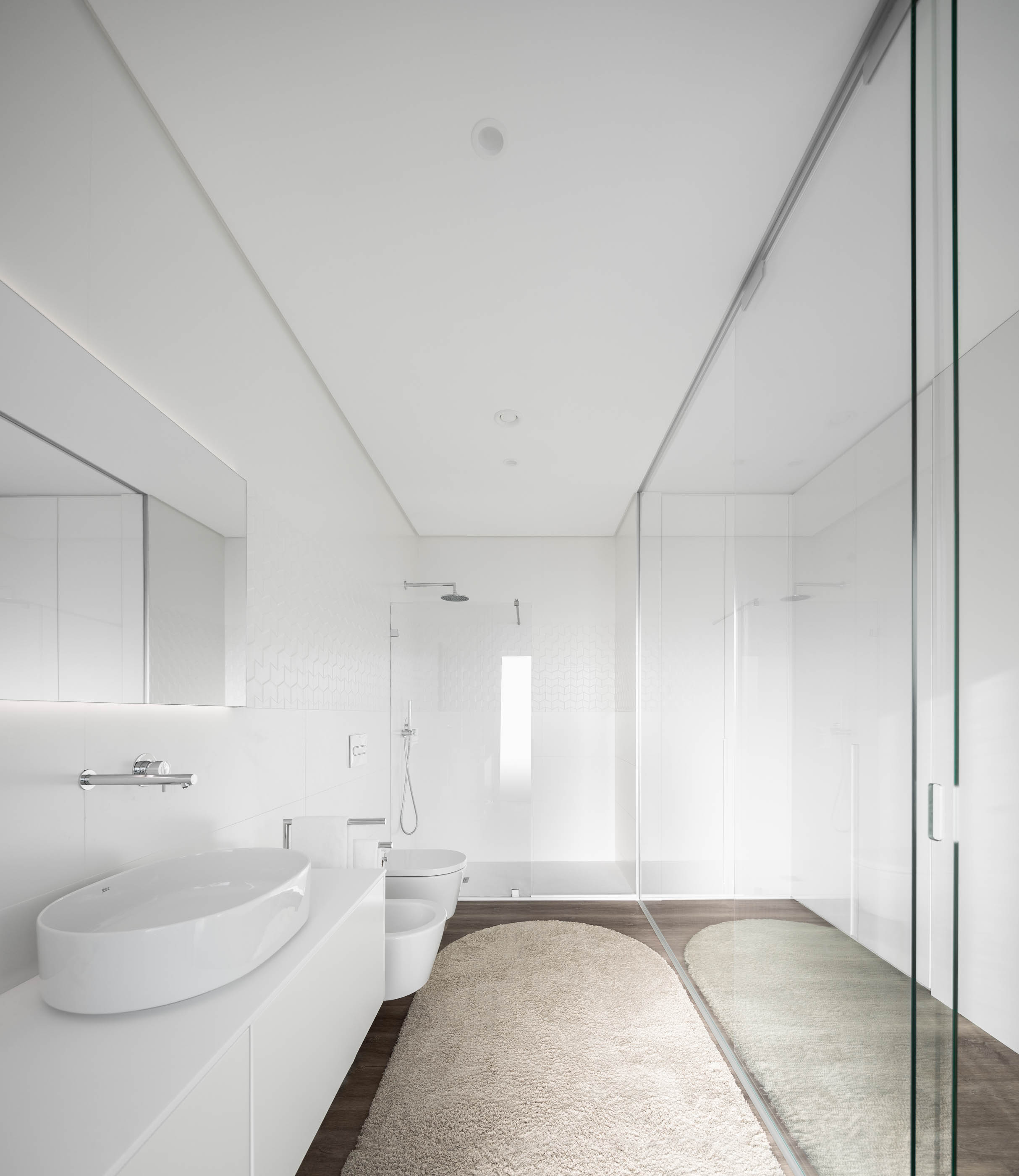 Casa de banho moderna com duche em vidro, lavatório branco e revestimento cerâmico branco texturizado. — Reabilitação Casa J arquitetura Frari em Portugal