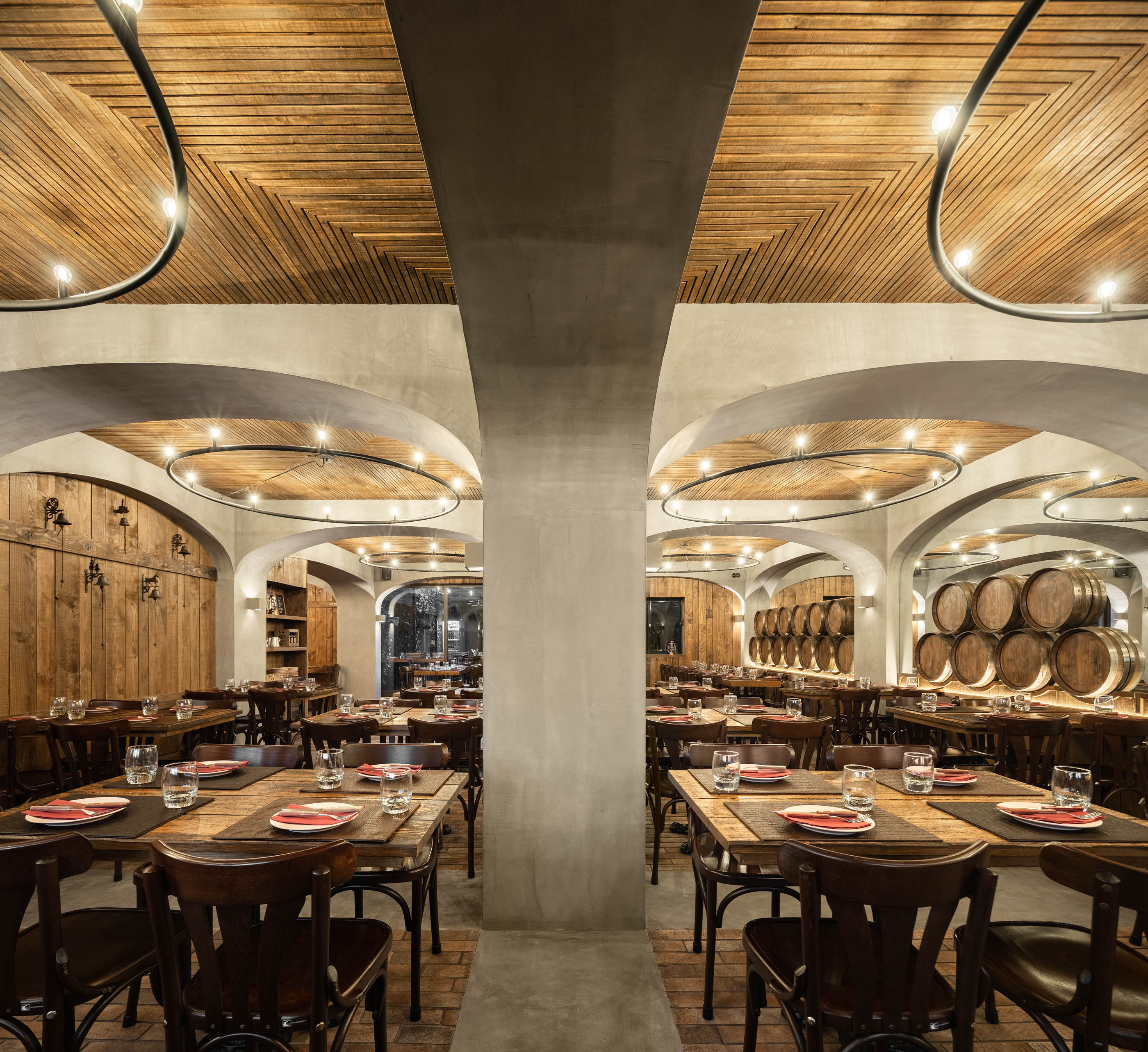 Visão simétrica do restaurante com mesas dispostas, teto em madeira, arcos em betão e iluminação circular. — Restaurante Barril arquitetura Paulo Merlini Architects em Portugal