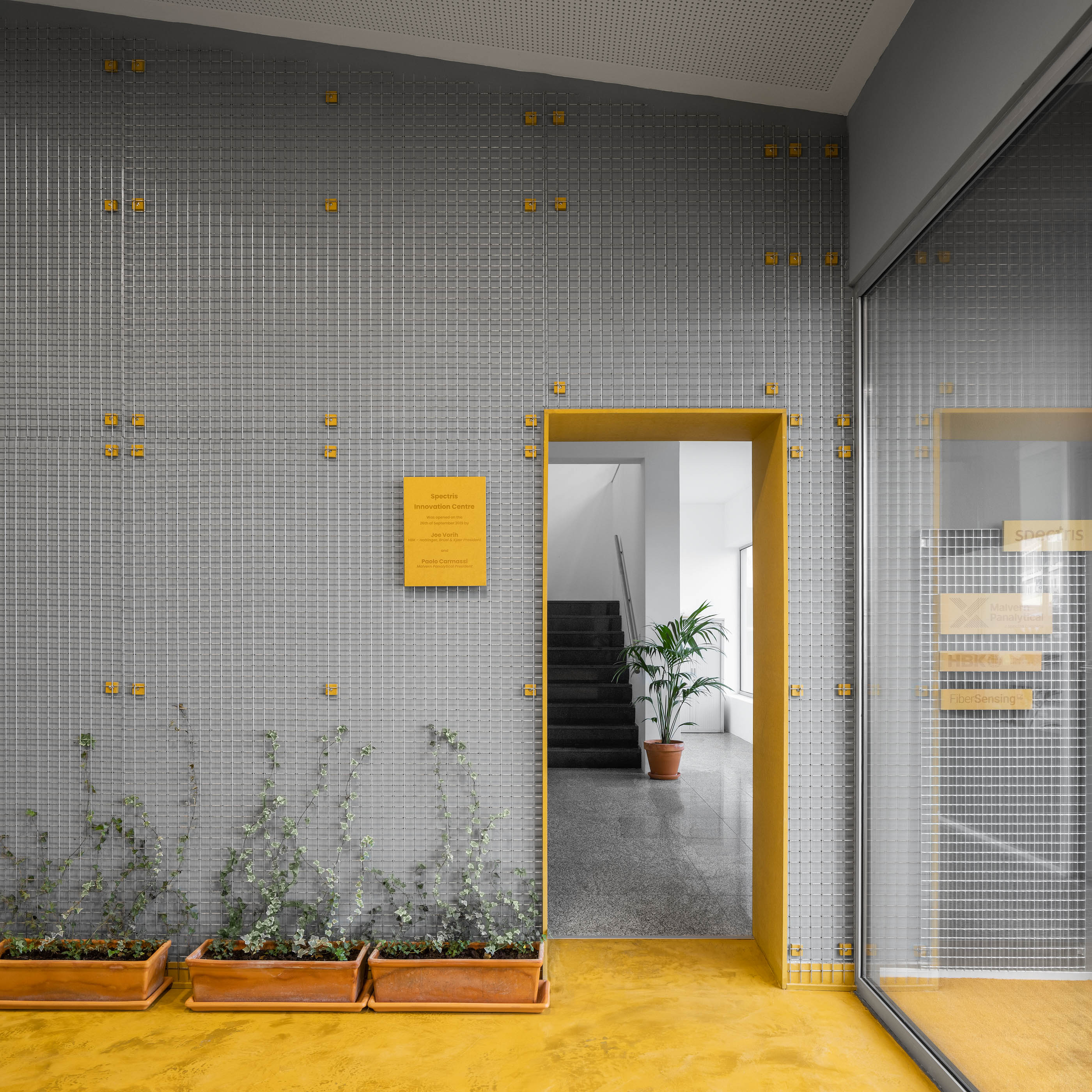 Divisão interior: Parede cinzenta revestida a mosaicos, porta amarela, plantas e chão amarelo, estilo industrial e minimalista. — HBK Spectris Innovation Centre arquitetura Studium Creative Studio em Porto