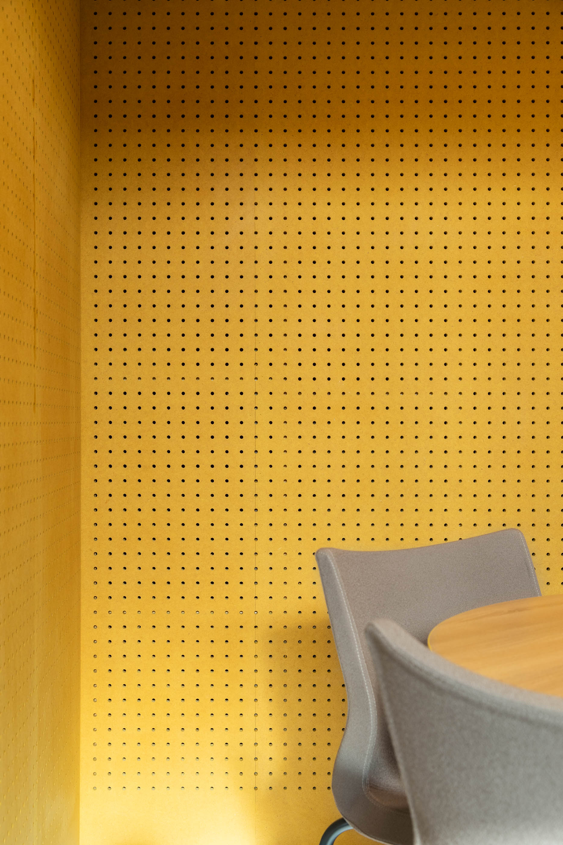 Detalhe: Interior de contentor com parede amarela perfurada, mesa redonda e cadeiras cinzentas, iluminação suave. — HBK Spectris Innovation Centre arquitetura Studium Creative Studio em Porto