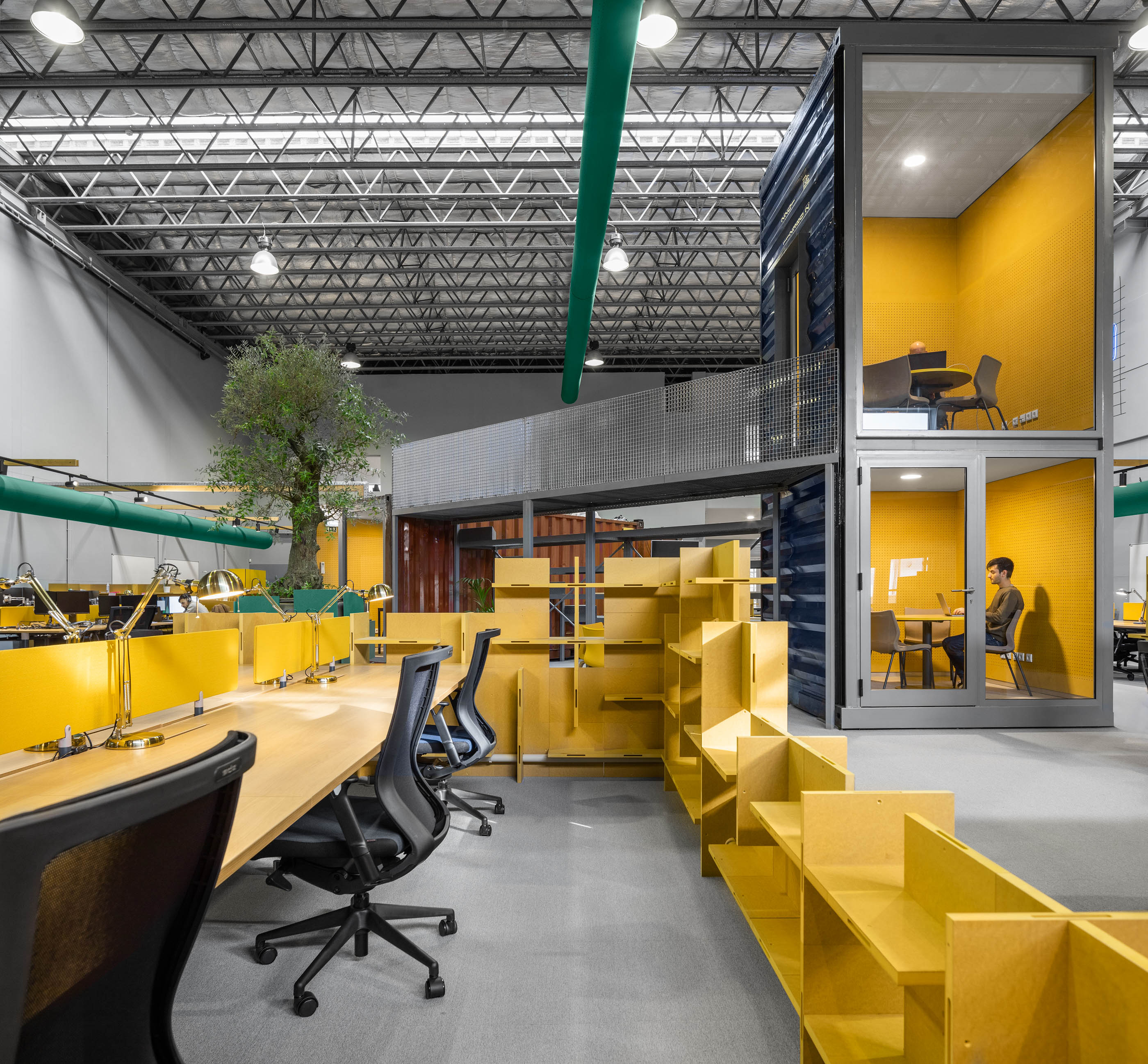 Espaço amplo: Escritórios com contentores sobrepostos, secretárias amarelas, estantes e uma árvore no centro. — HBK Spectris Innovation Centre arquitetura Studium Creative Studio em Porto