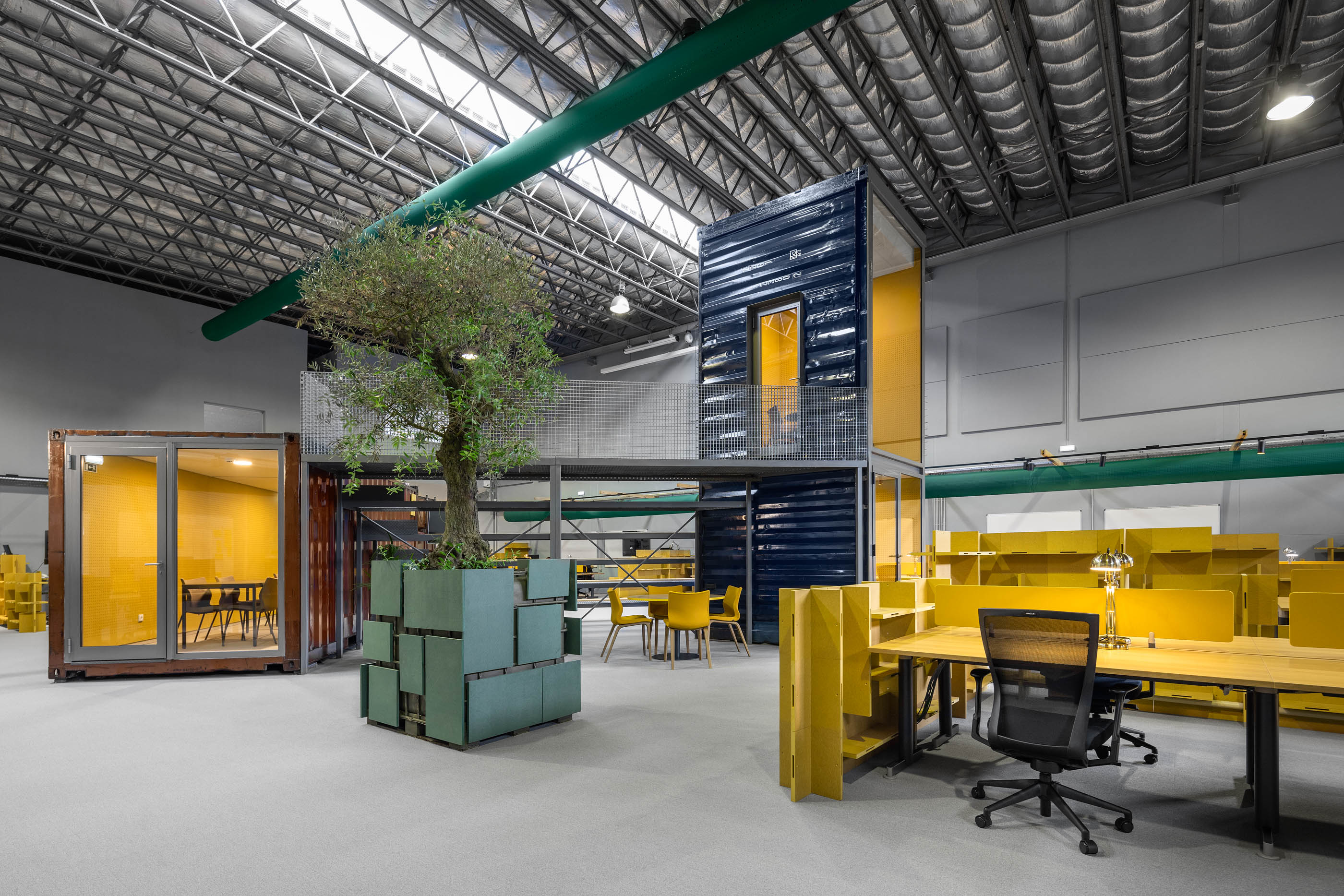 Espaço amplo: Vista geral com contentores, árvore central, secretárias amarelas e iluminação industrial. — HBK Spectris Innovation Centre arquitetura Studium Creative Studio em Porto
