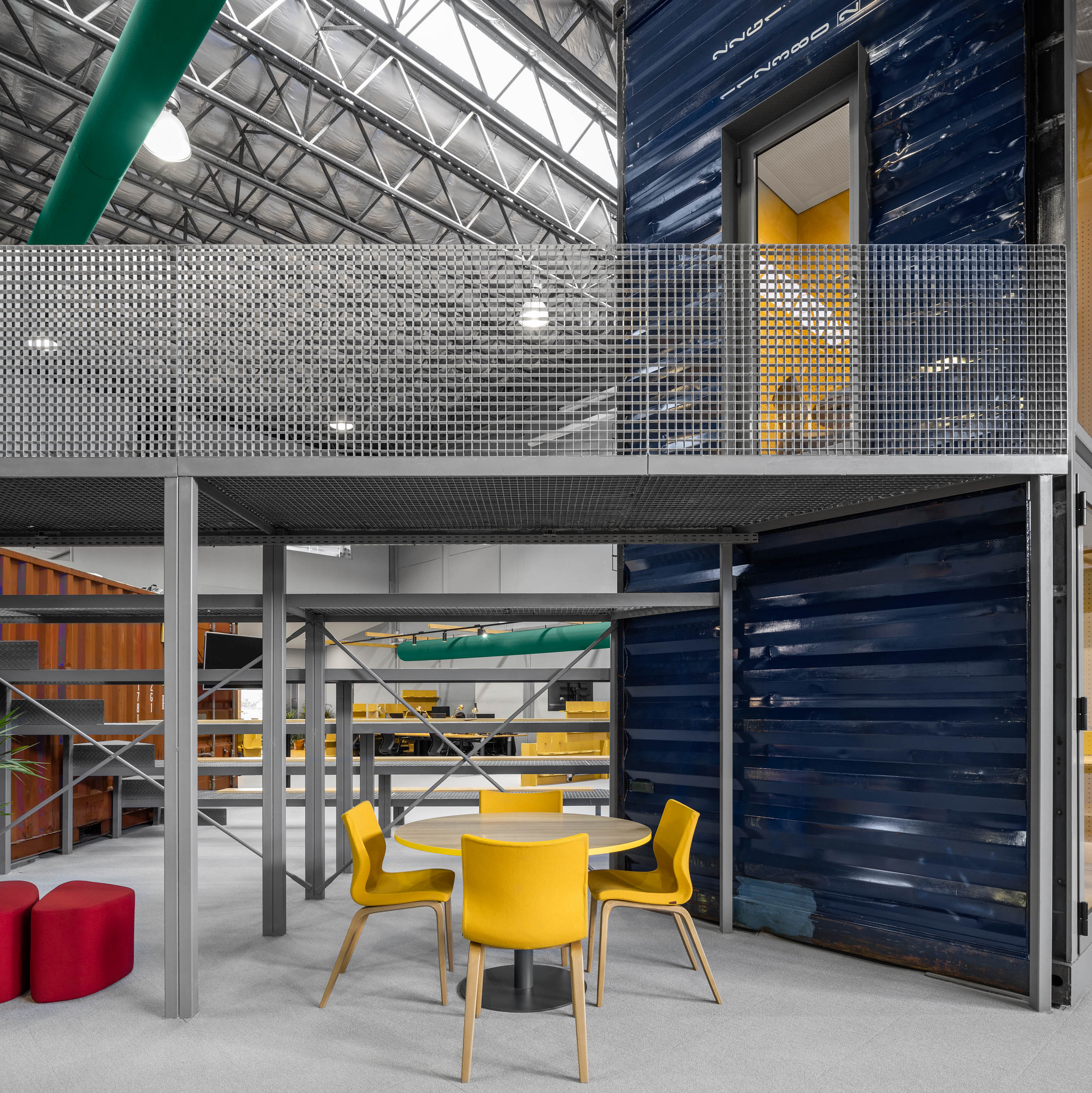Espaço amplo: Detalhe de contentores sobrepostos, escadas metálicas, mobiliário amarelo e iluminação industrial. — HBK Spectris Innovation Centre arquitetura Studium Creative Studio em Porto