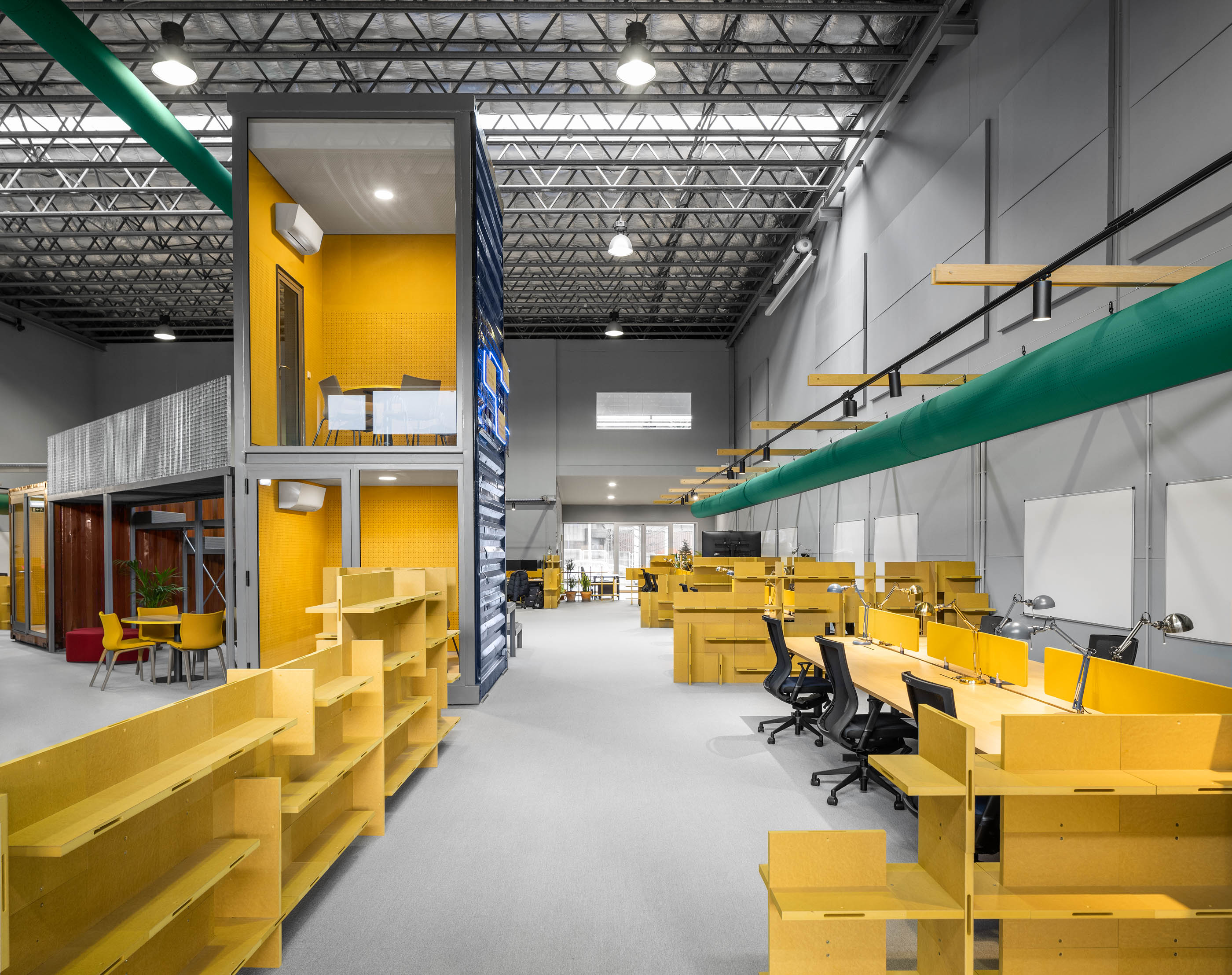 Espaço amplo: Vista longitudinal com contentores, secretárias amarelas, estantes e iluminação industrial. — HBK Spectris Innovation Centre arquitetura Studium Creative Studio em Porto