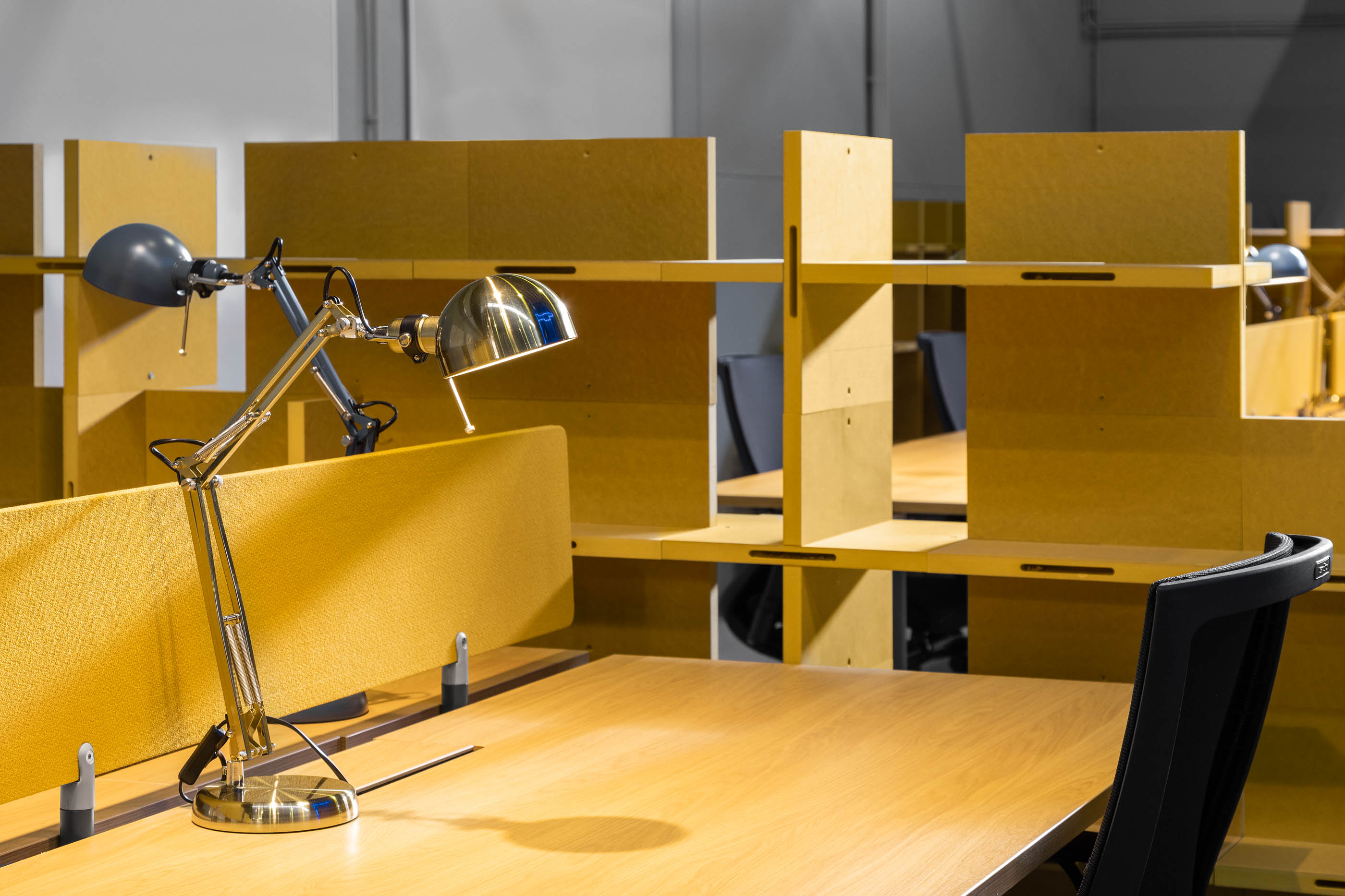 Detalhe: Secretária de madeira com divisória amarela, estante modular e candeeiro de metal. — HBK Spectris Innovation Centre arquitetura Studium Creative Studio em Porto