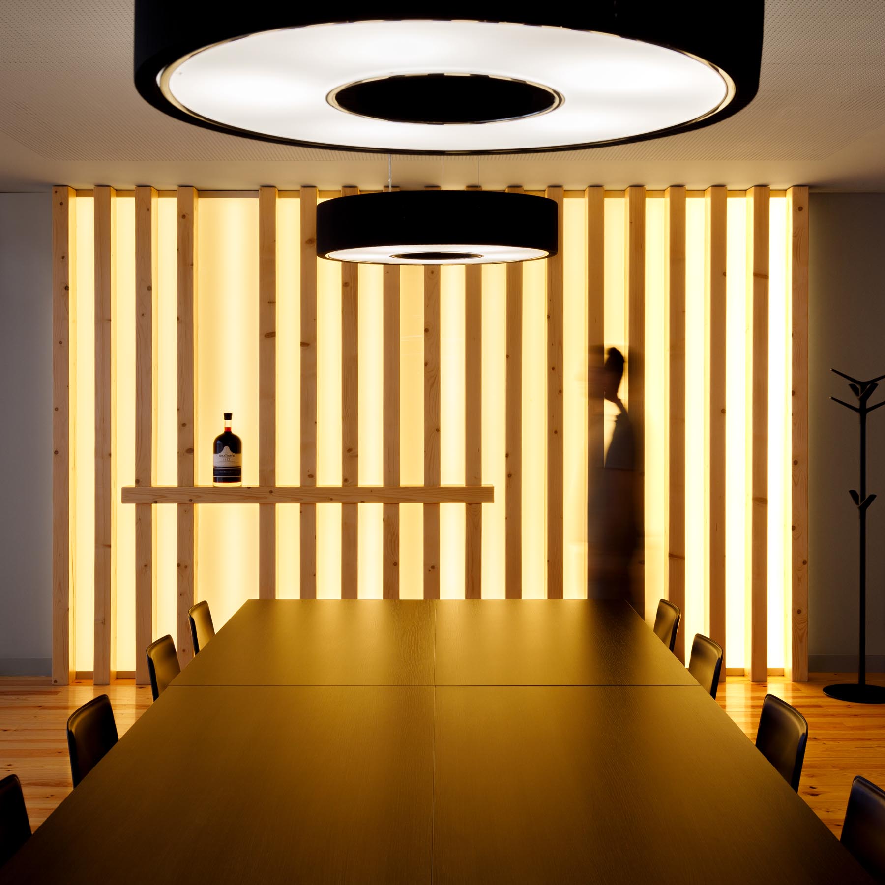 Sala de reuniões com mesa escura, cadeiras pretas e painel de ripas de madeira iluminadas ao fundo. — Portfolio Vinhos arquitetura Studium Creative Studio em Vila Nova de Gaia