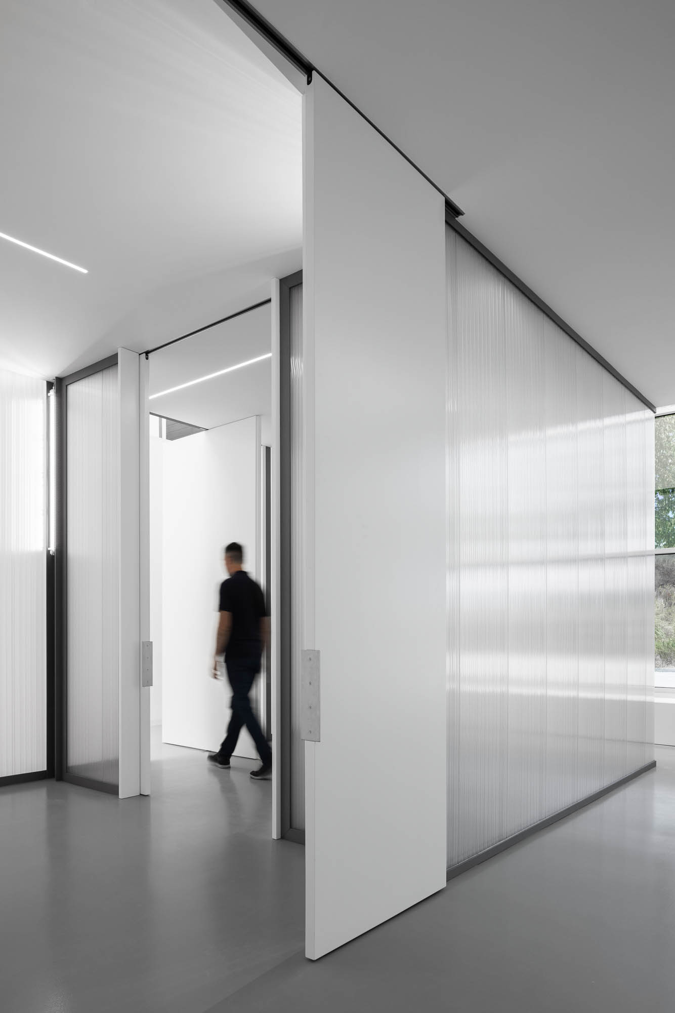 Corredor com portas deslizantes brancas e paredes em policarbonato translúcido, iluminação linear no teto. — Escritórios MA arquitetura éOp – arquitectura e design em Maia