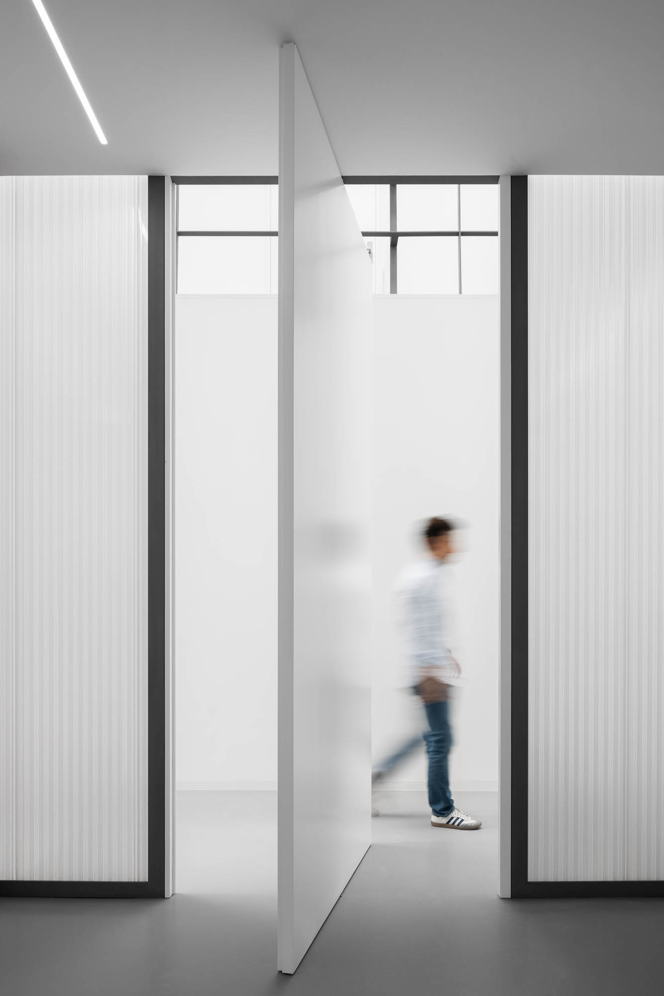 Porta pivotante branca semi-aberta, ladeada por paredes em policarbonato translúcido com estrutura metálica preta. — Escritórios MA arquitetura éOp – arquitectura e design em Maia
