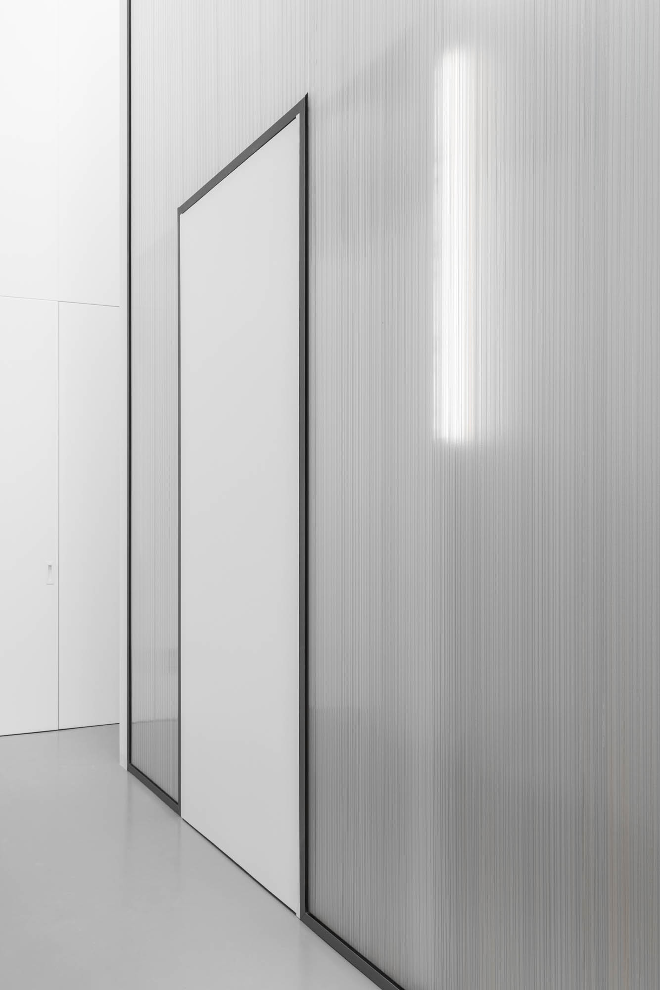 Detalhe de parede em policarbonato translúcido com estrutura preta, porta branca e parede branca ao fundo. — Escritórios MA arquitetura éOp – arquitectura e design em Maia