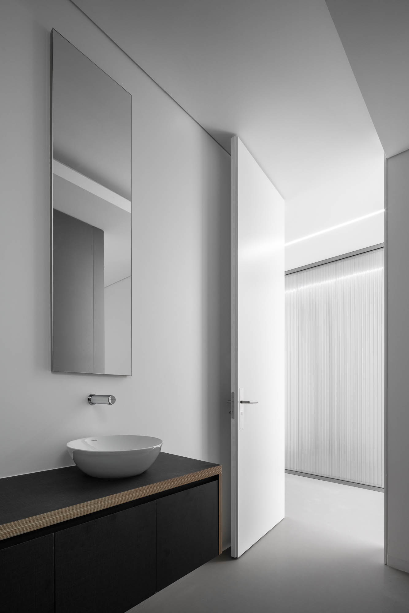 Casa de banho com lavatório branco, espelho vertical e porta branca aberta para corredor com paredes em policarbonato. — Escritórios MA arquitetura éOp – arquitectura e design em Maia