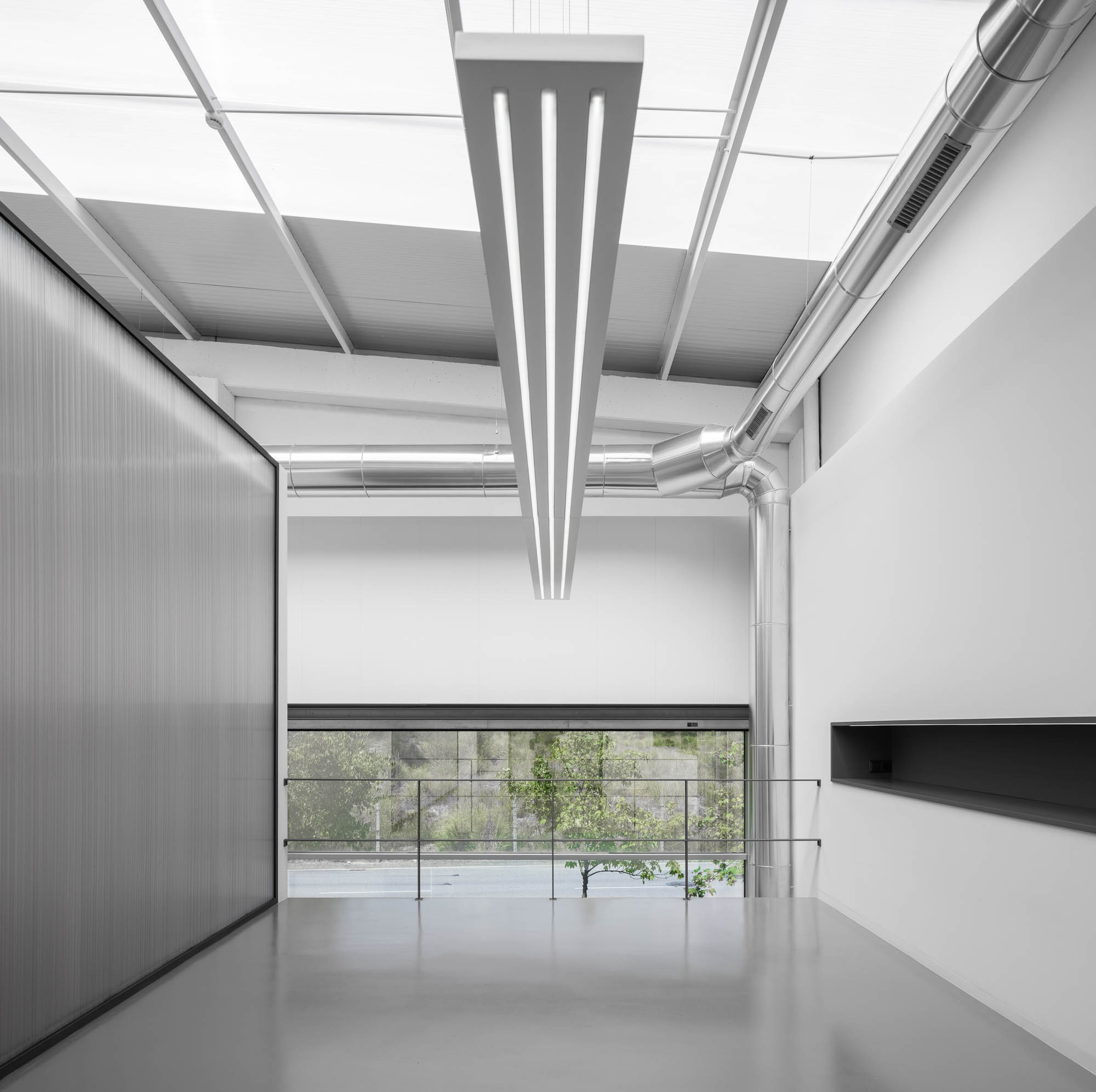 Espaço amplo com chão cinzento, parede revestida a painéis metálicos, iluminação linear e tubagens expostas no teto. — Escritórios MA arquitetura éOp – arquitectura e design em Maia