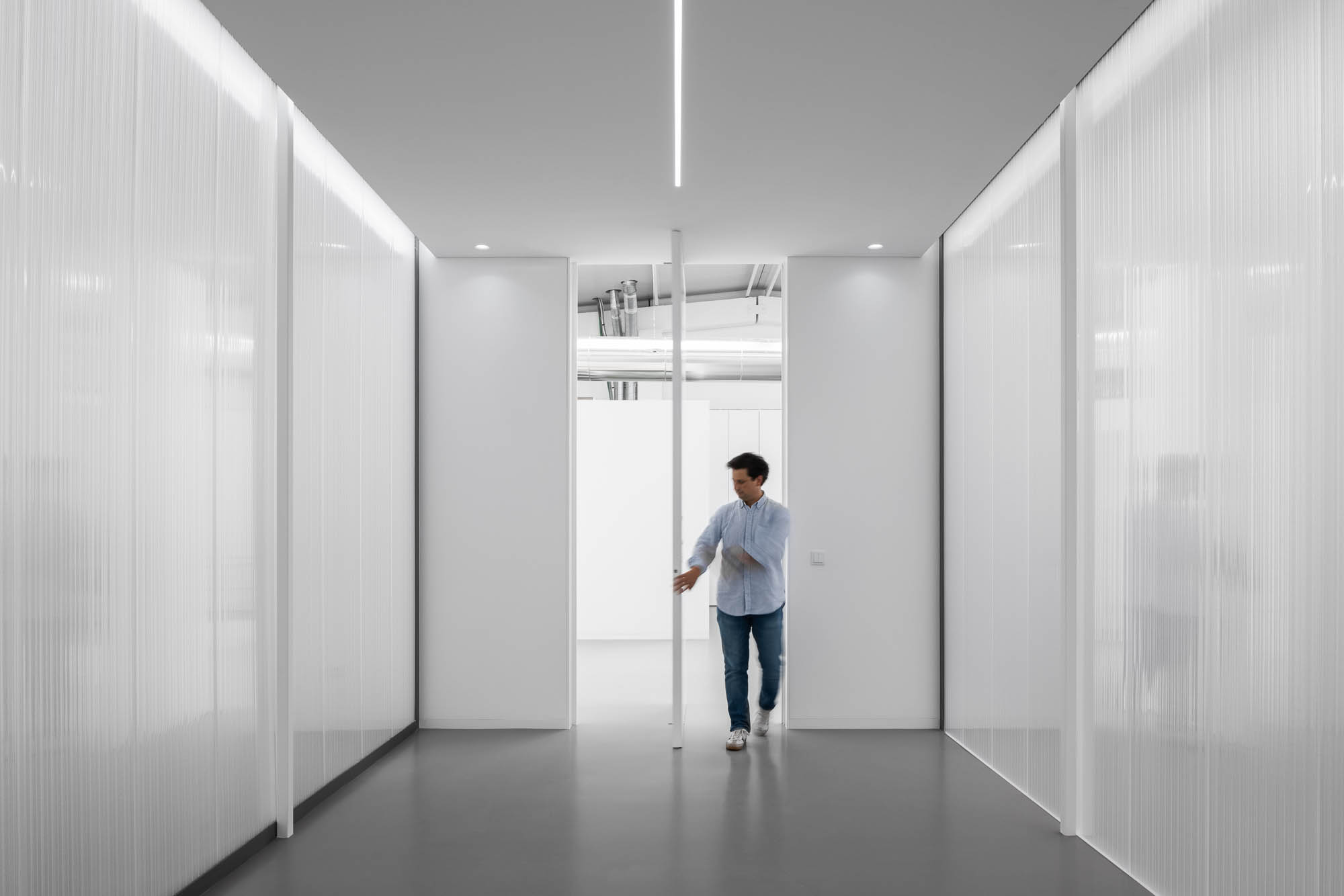 Corredor com paredes em policarbonato translúcido, porta pivotante branca e iluminação linear no teto. — Escritórios MA arquitetura éOp – arquitectura e design em Maia