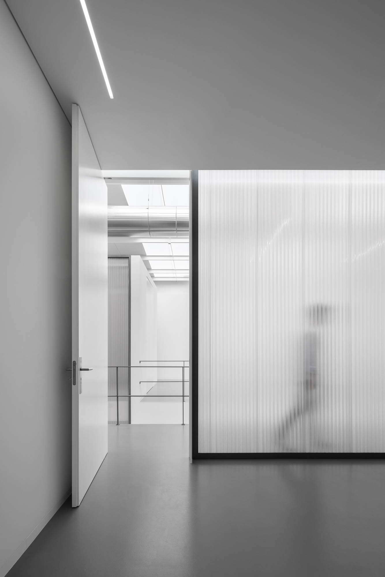 Perspectiva de corredor com porta branca aberta, parede em policarbonato translúcido e guarda-corpo metálico ao fundo. — Escritórios MA arquitetura éOp – arquitectura e design em Maia
