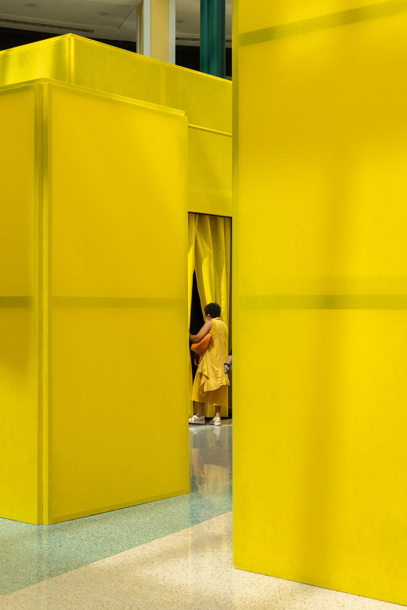 Detalhe de cubos amarelos translúcidos, com uma pessoa a entrar numa divisão através de uma cortina. — Museu Temporário Nadir Afonso arquitetura Diogo Aguiar Studio em Lisboa