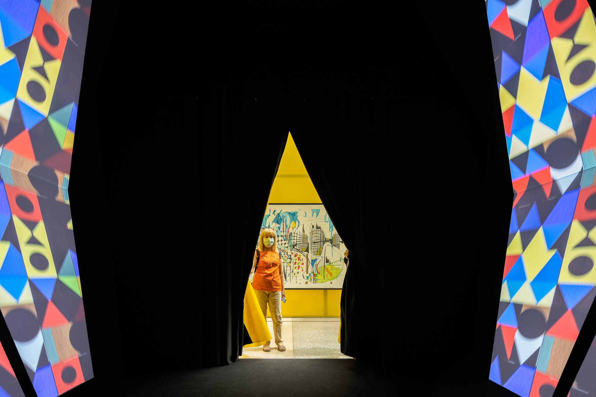 Entrada para uma sala escura com cortinas pretas, revelando uma parede amarela e uma obra de arte. — Museu Temporário Nadir Afonso arquitetura Diogo Aguiar Studio em Lisboa