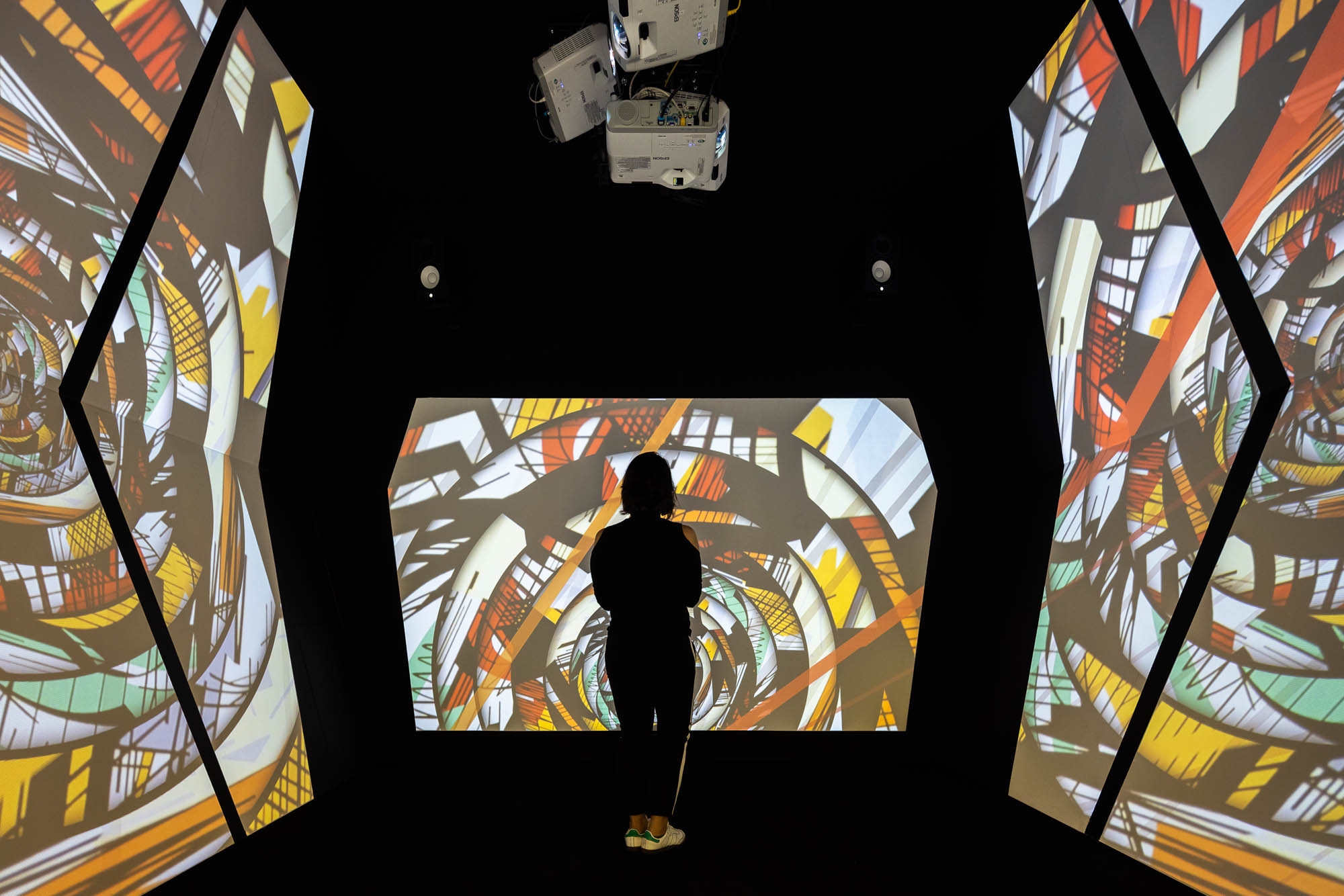 Interior de sala escura com projeções de obras de arte nas paredes e uma visitante a observar. — Museu Temporário Nadir Afonso arquitetura Diogo Aguiar Studio em Lisboa