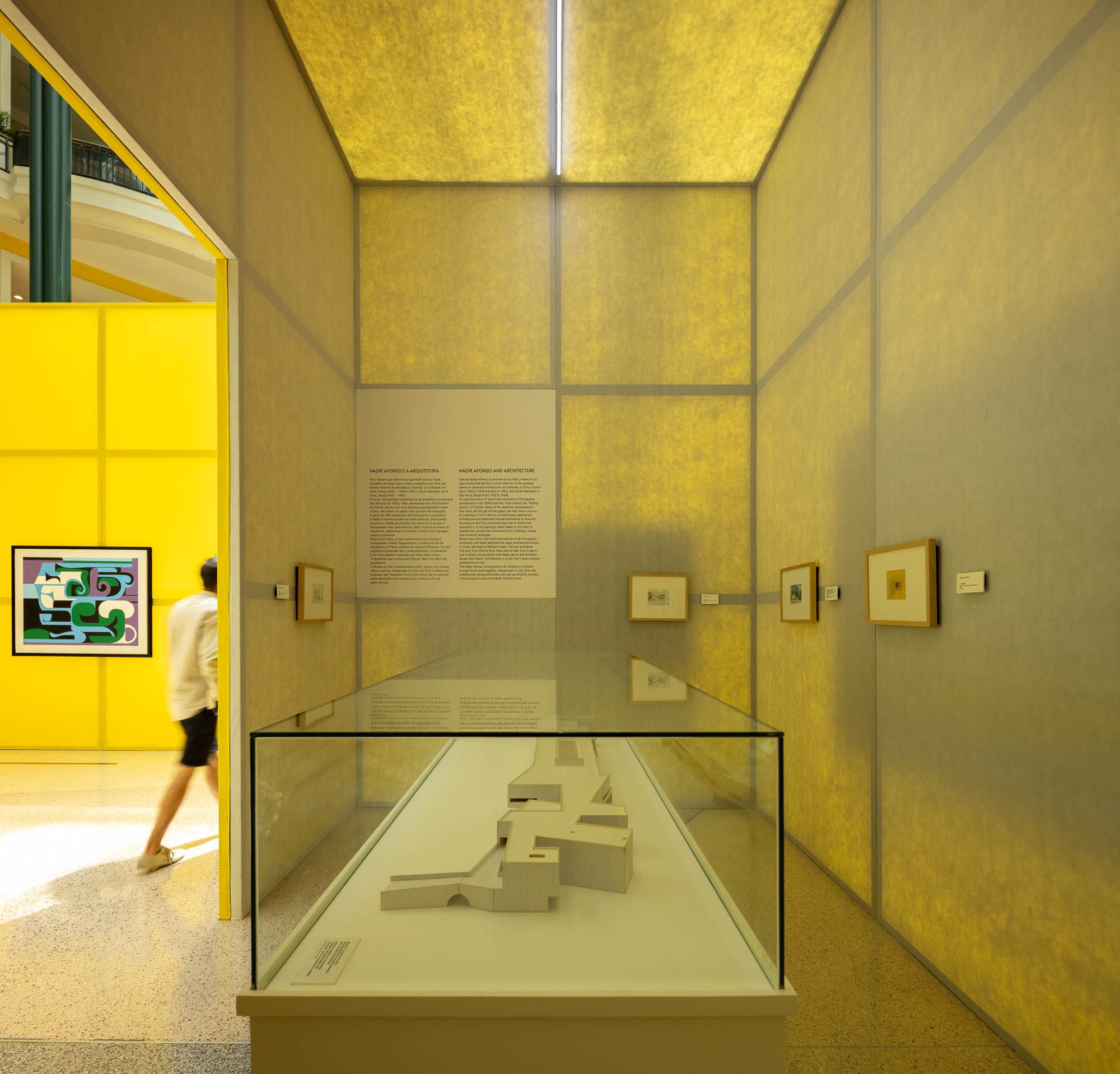 Interior de um cubo amarelo, com uma vitrine contendo uma maquete e painéis informativos nas paredes. — Museu Temporário Nadir Afonso arquitetura Diogo Aguiar Studio em Lisboa