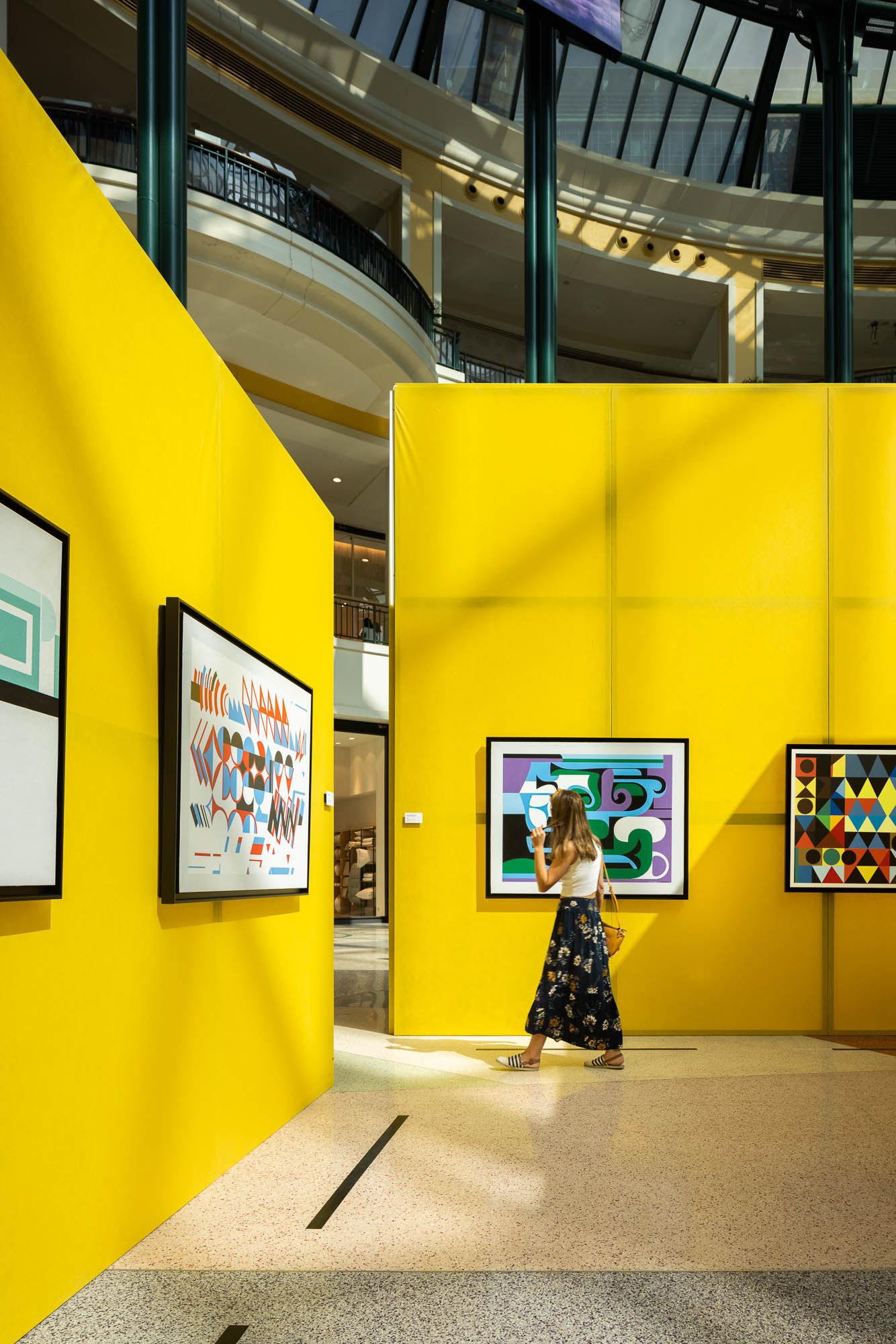 Corredor entre painéis amarelos, com obras de arte em exibição e uma visitante a percorrer o espaço. — Museu Temporário Nadir Afonso arquitetura Diogo Aguiar Studio em Lisboa