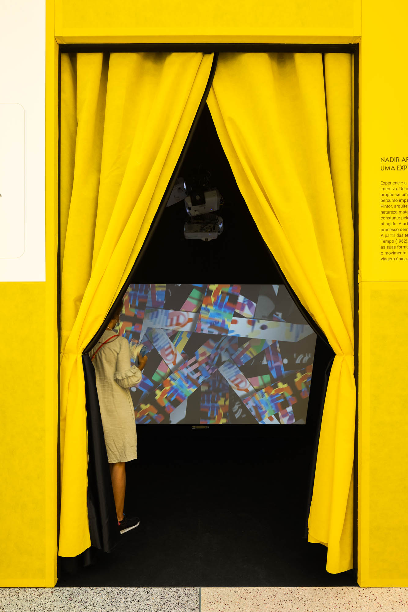 Entrada para uma sala de projeção com cortinas amarelas e pretas, e uma pessoa a espreitar. — Museu Temporário Nadir Afonso arquitetura Diogo Aguiar Studio em Lisboa