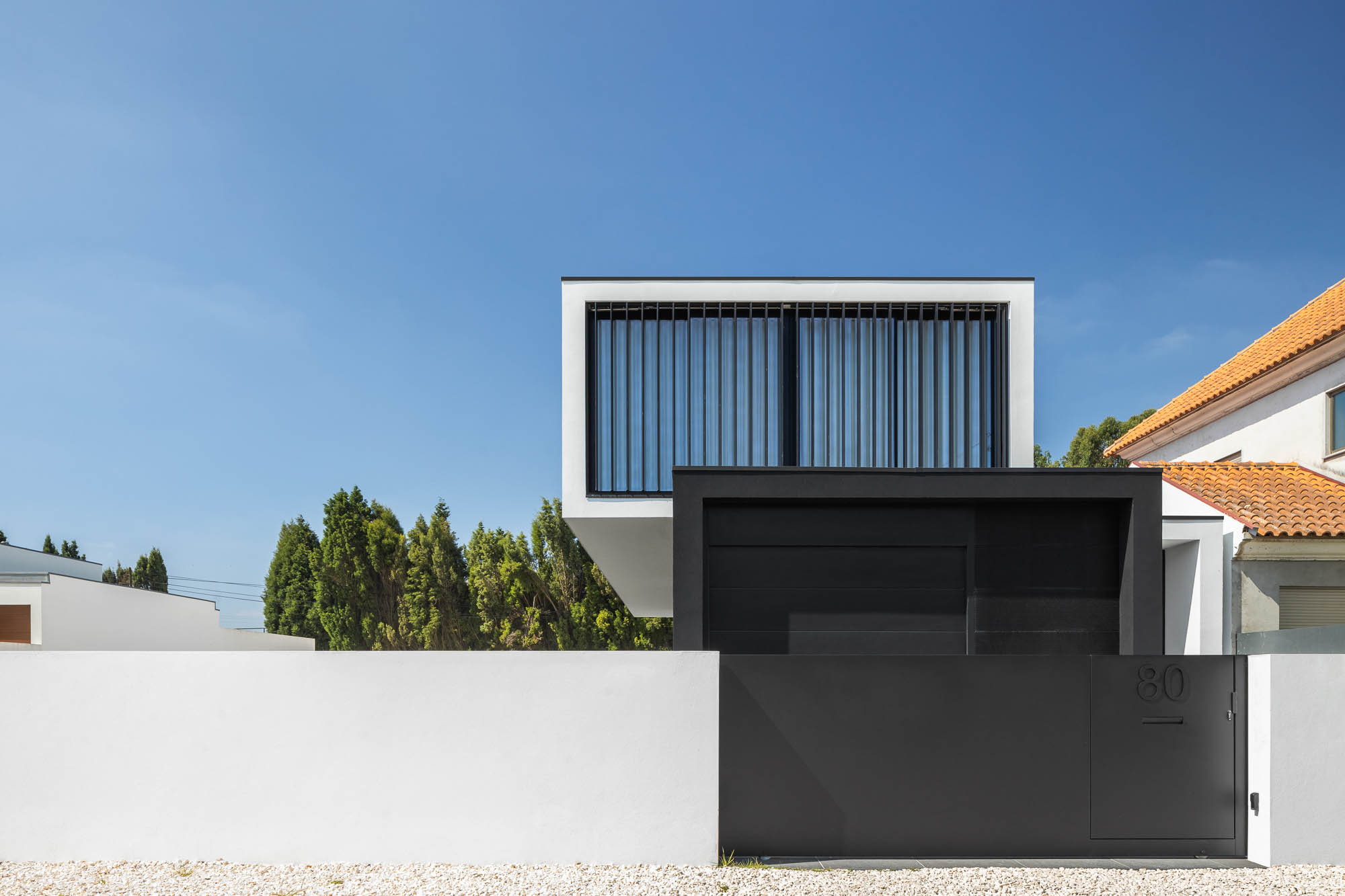 Fachada minimalista da casa com volume branco sobreposto a estrutura preta, portão e muro branco. — Casa Diagonal arquitetura Frari em Aveiro