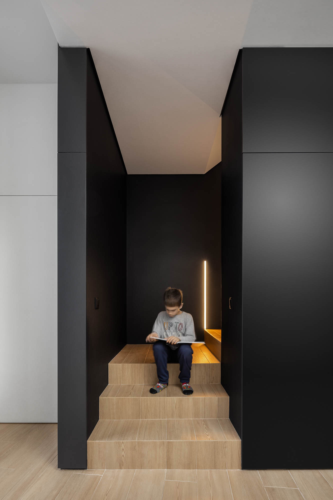 Escada interior em madeira clara com criança sentada, paredes pretas e armários embutidos. — Casa Diagonal arquitetura Frari em Aveiro