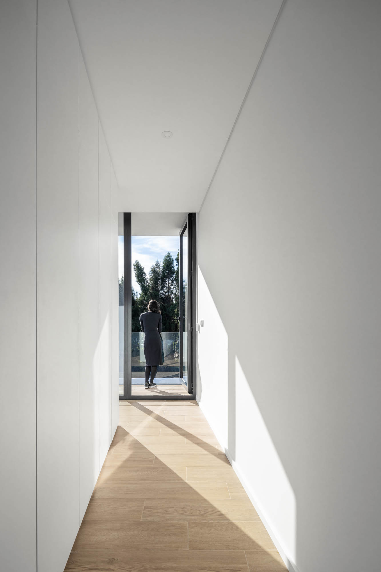 Corredor branco com pavimento em madeira, armários embutidos e porta para varanda. — Casa Diagonal arquitetura Frari em Aveiro