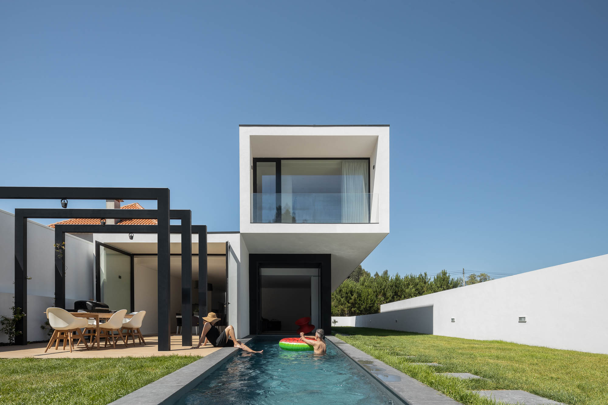 Exterior da casa com piscina, pérgola preta, área de refeições e volume branco suspenso. — Casa Diagonal arquitetura Frari em Aveiro