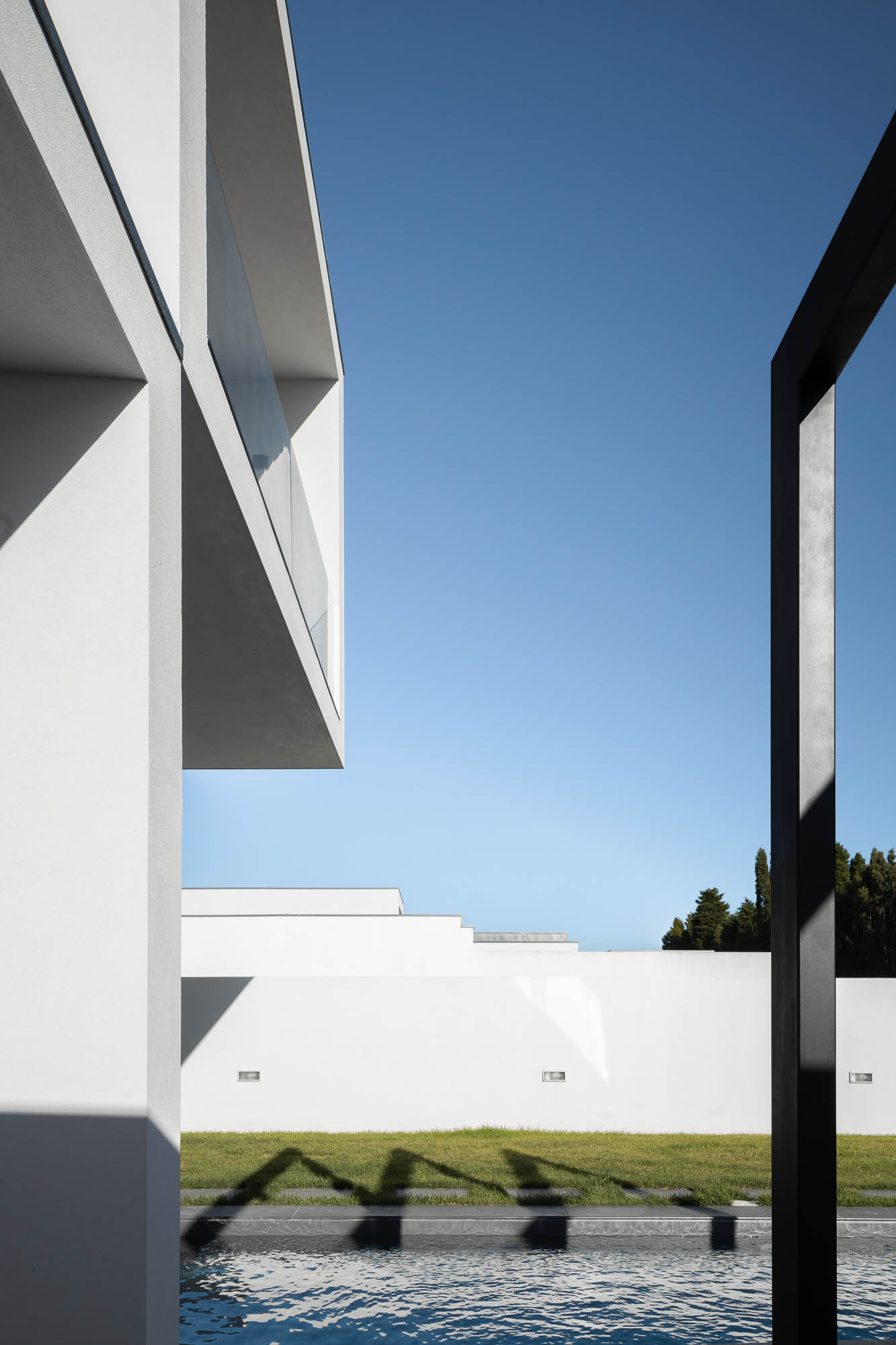 Pormenor da arquitetura minimalista com piscina, relvado e muro branco ao fundo. — Casa Diagonal arquitetura Frari em Aveiro