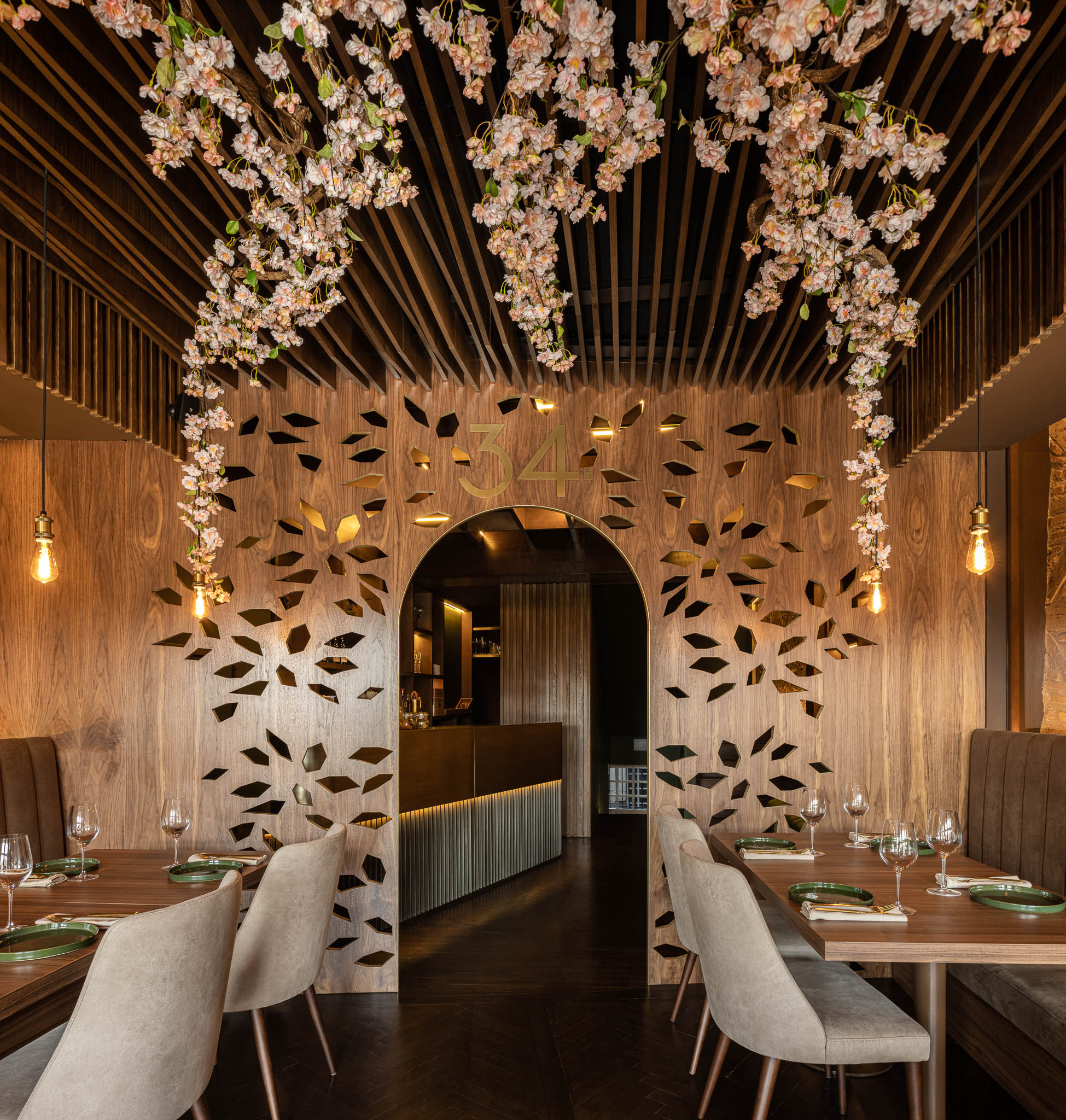 Entrada do restaurante com painel de madeira recortado com o número "34", iluminação pendente e decoração floral. — Restaurante 34 arquitetura REM'A Arquitectos em Guimarães