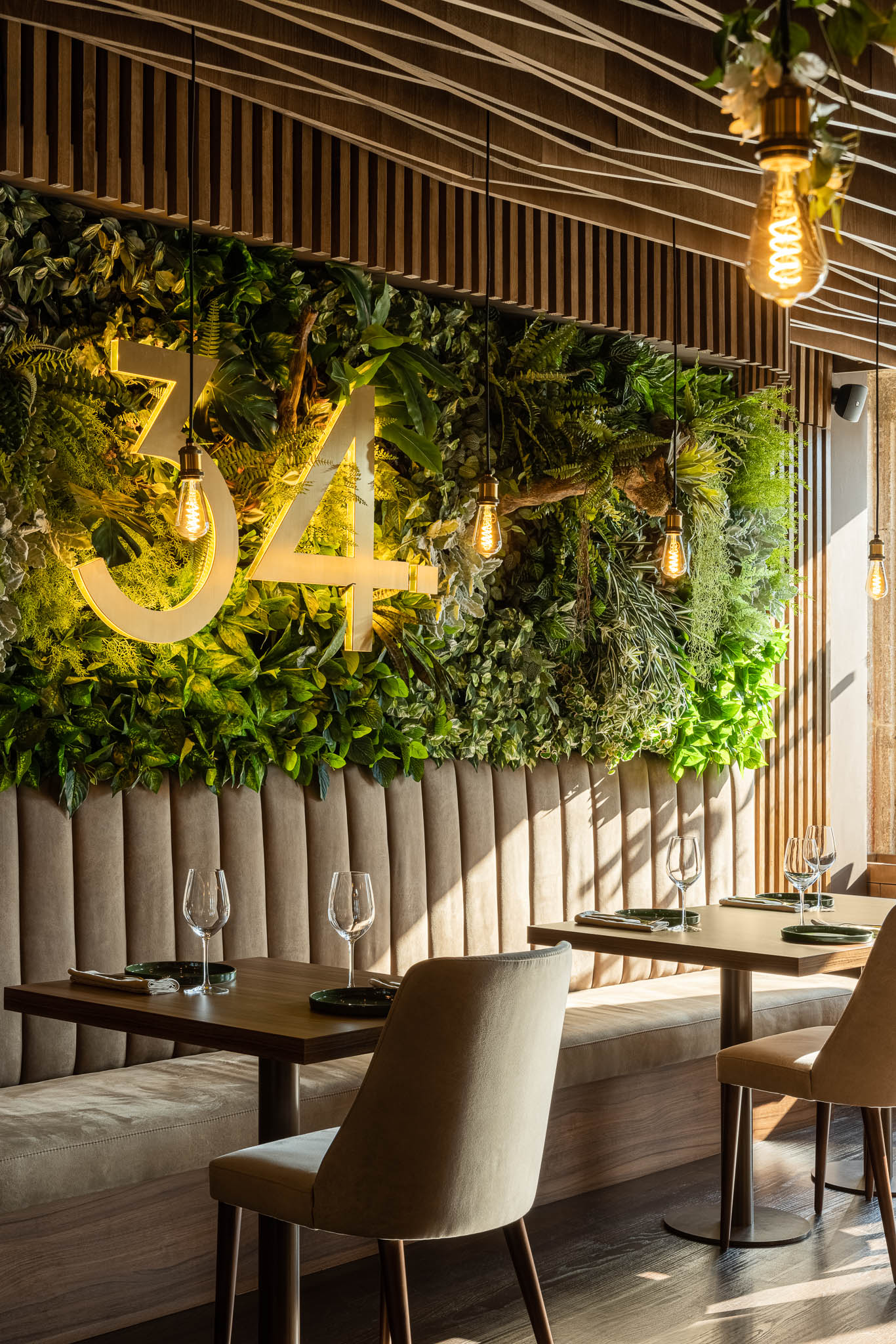 Parede verde vertical com o número "34" iluminado, mesas de madeira, cadeiras neutras e iluminação pendente. — Restaurante 34 arquitetura REM'A Arquitectos em Guimarães