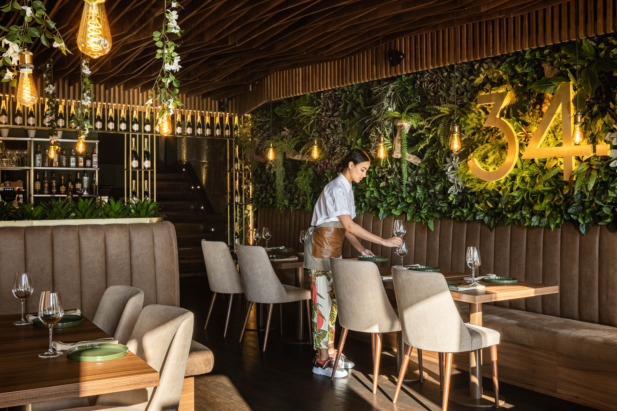 Interior do restaurante com mesas, cadeiras, sofás, parede verde com o número "34" e iluminação suave. — Restaurante 34 arquitetura REM'A Arquitectos em Guimarães