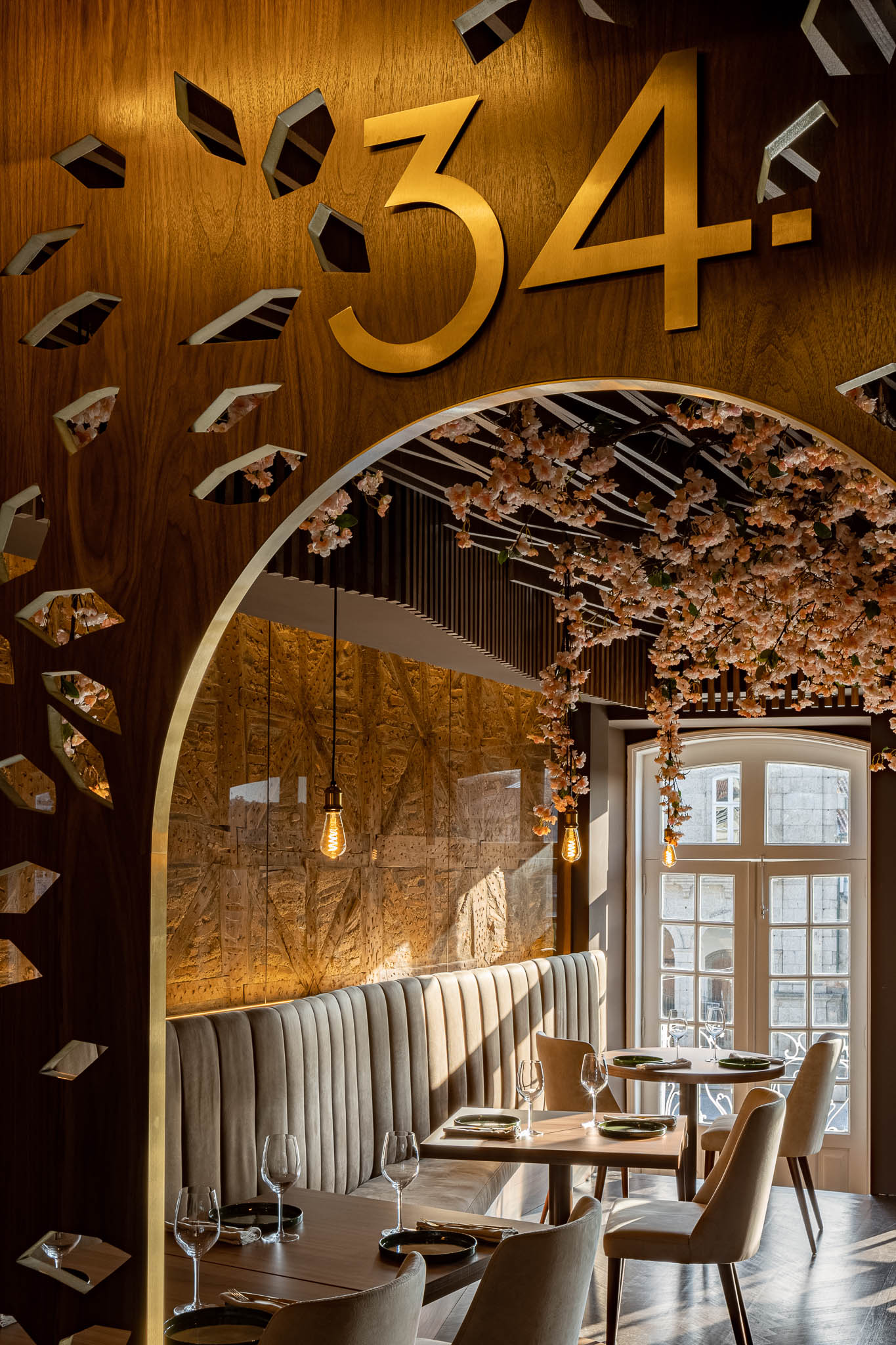 Detalhe da parede com o número "34" dourado, painel de madeira recortado e decoração floral suspensa. — Restaurante 34 arquitetura REM'A Arquitectos em Guimarães