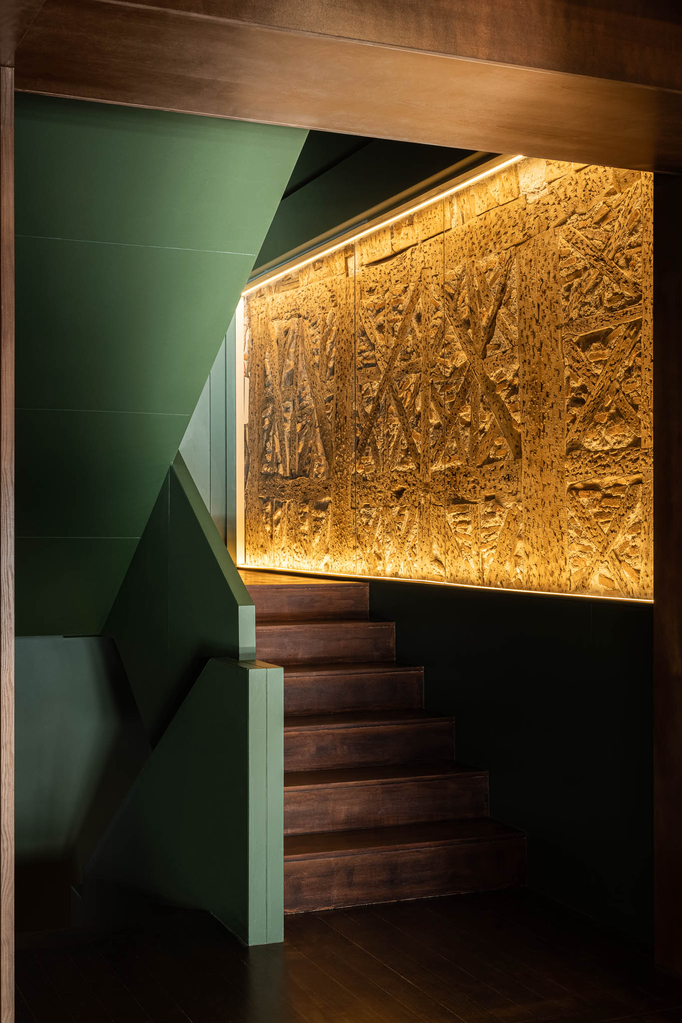 Escadas de madeira escura com paredes verde-escuras e iluminação indireta, destacando uma parede texturizada. — Restaurante 34 arquitetura REM'A Arquitectos em Guimarães