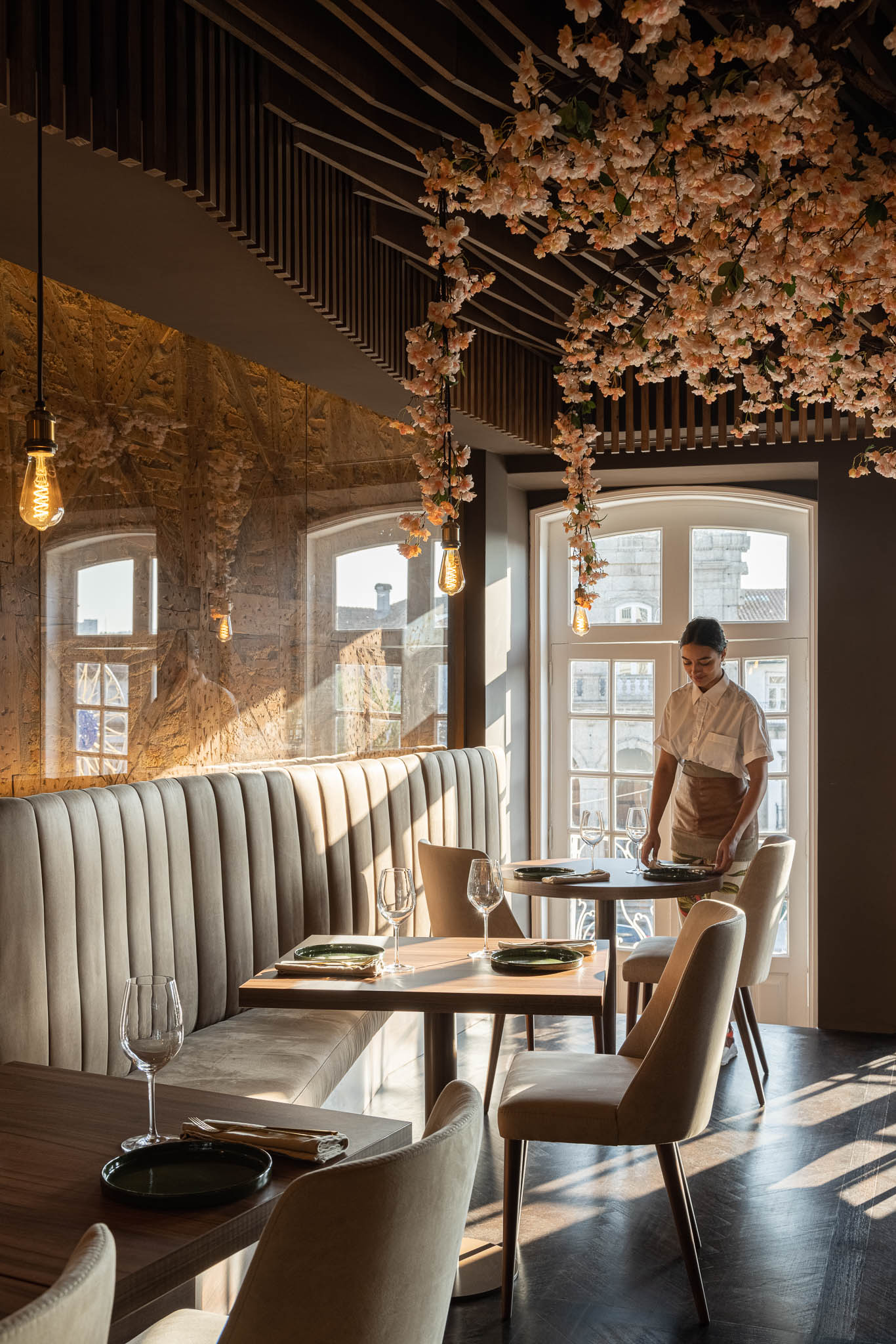 Sala de jantar com sofás de veludo, mesas de madeira, cadeiras neutras e uma parede de pedra texturizada. — Restaurante 34 arquitetura REM'A Arquitectos em Guimarães