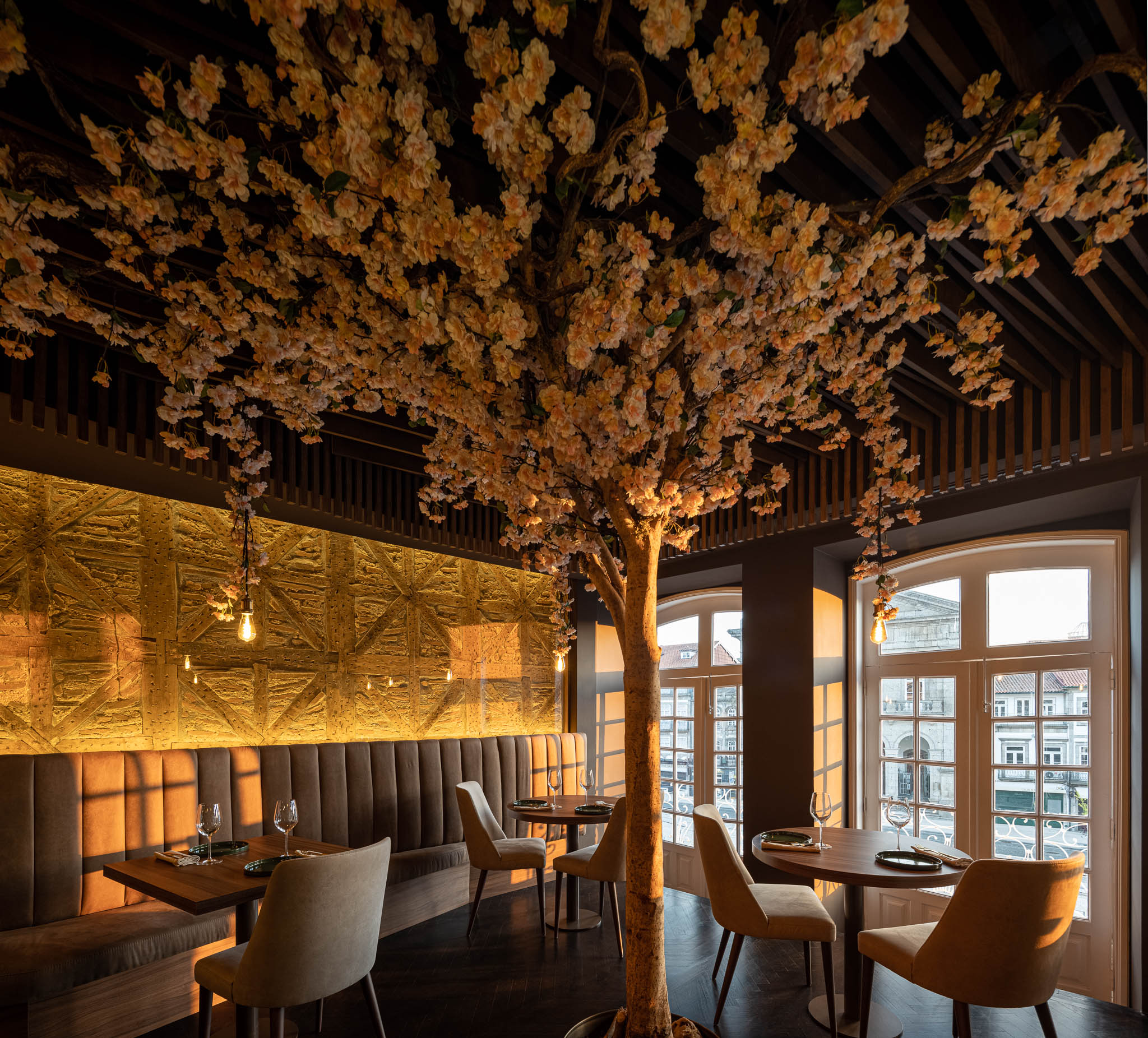 Espaço de refeições com árvore florida central, paredes cinzentas, janelas amplas e iluminação suave. — Restaurante 34 arquitetura REM'A Arquitectos em Guimarães