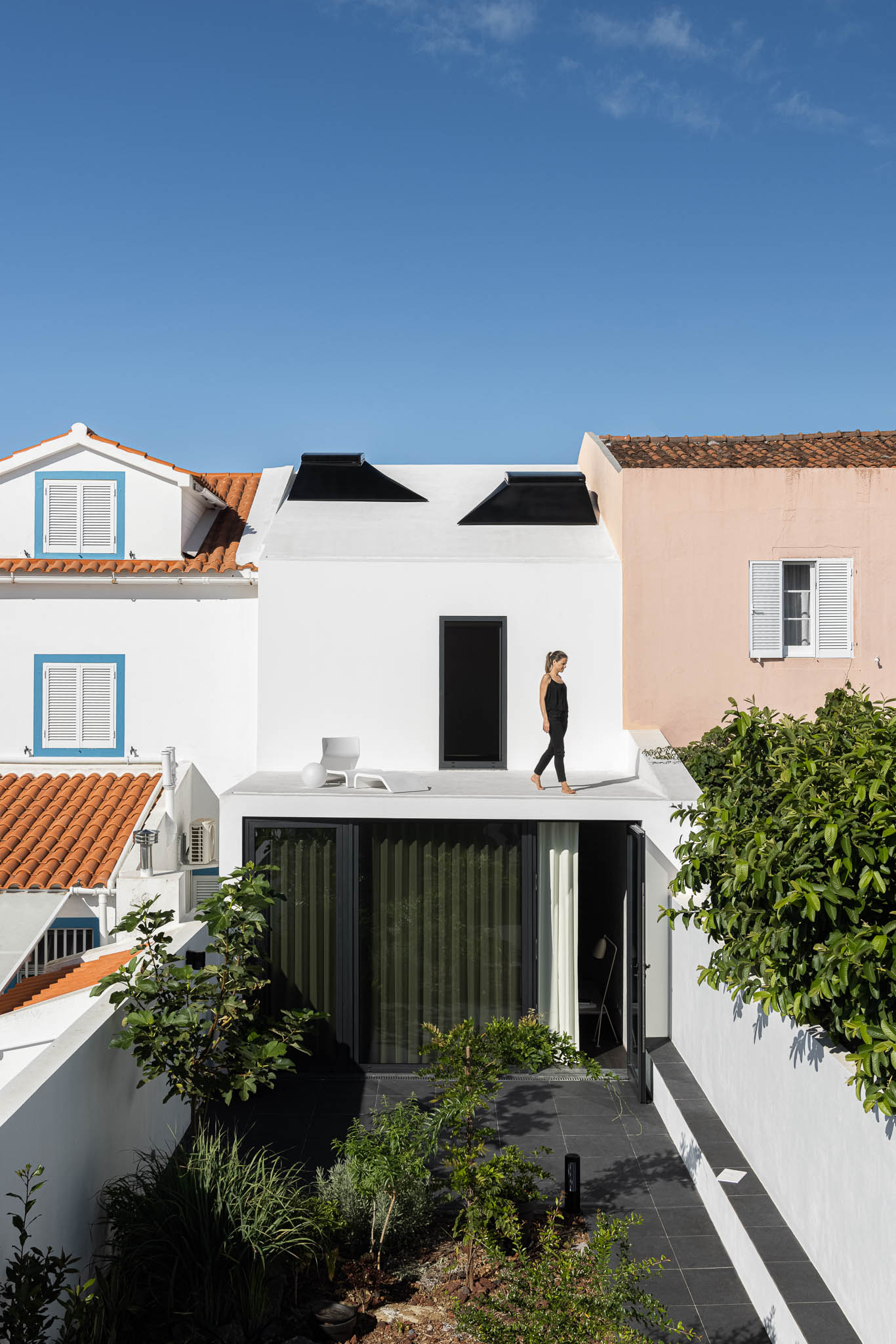 Vista exterior da casa com telhado branco, janelas pretas e jardim interior. Arquitetura moderna integrada no contexto urbano. — Casa moinho de vento arquitetura BOX arquitectos em Ponta Delgada