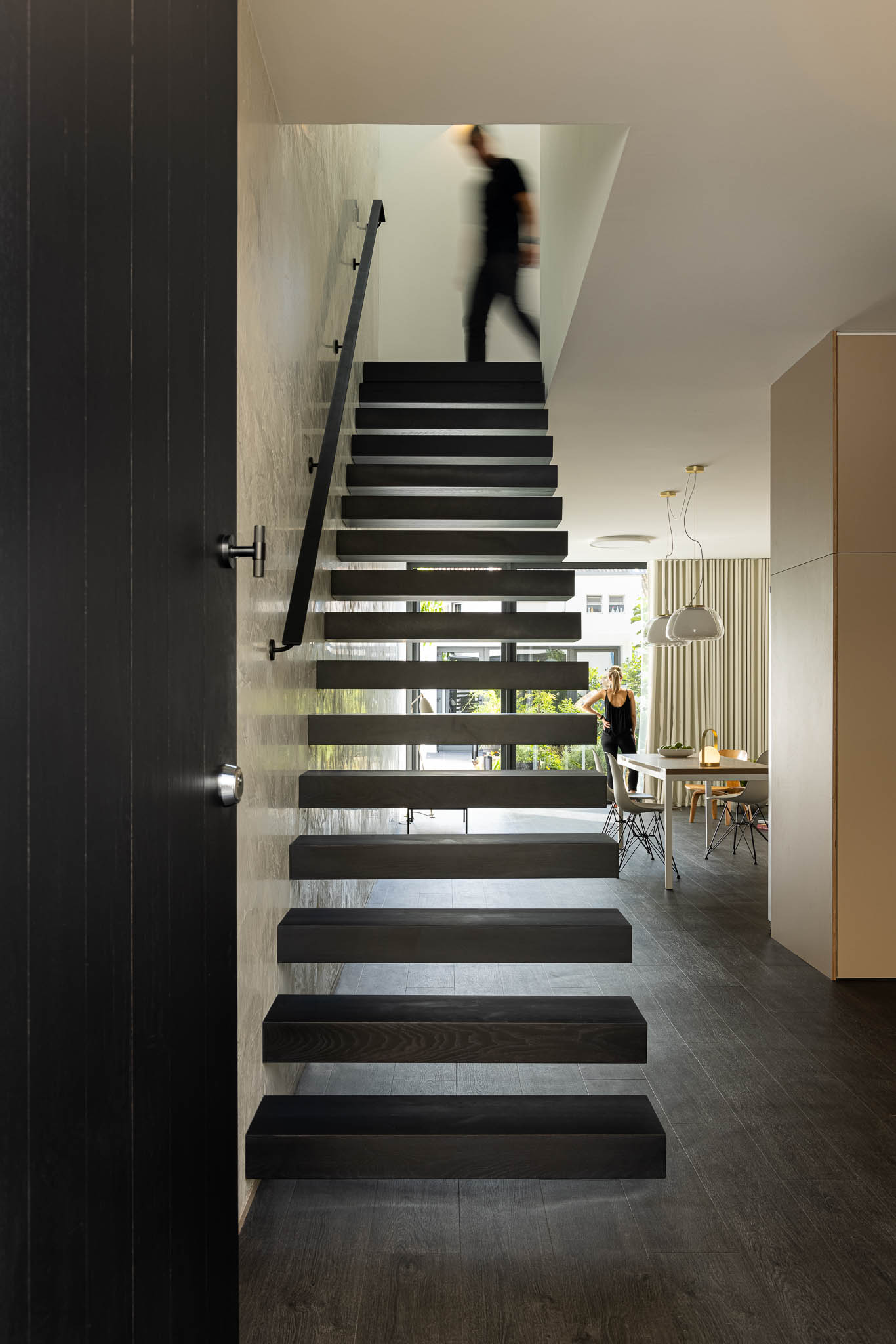 Escada suspensa preta com vista para a sala de jantar. Iluminação natural e design contemporâneo. — Casa moinho de vento arquitetura BOX arquitectos em Ponta Delgada