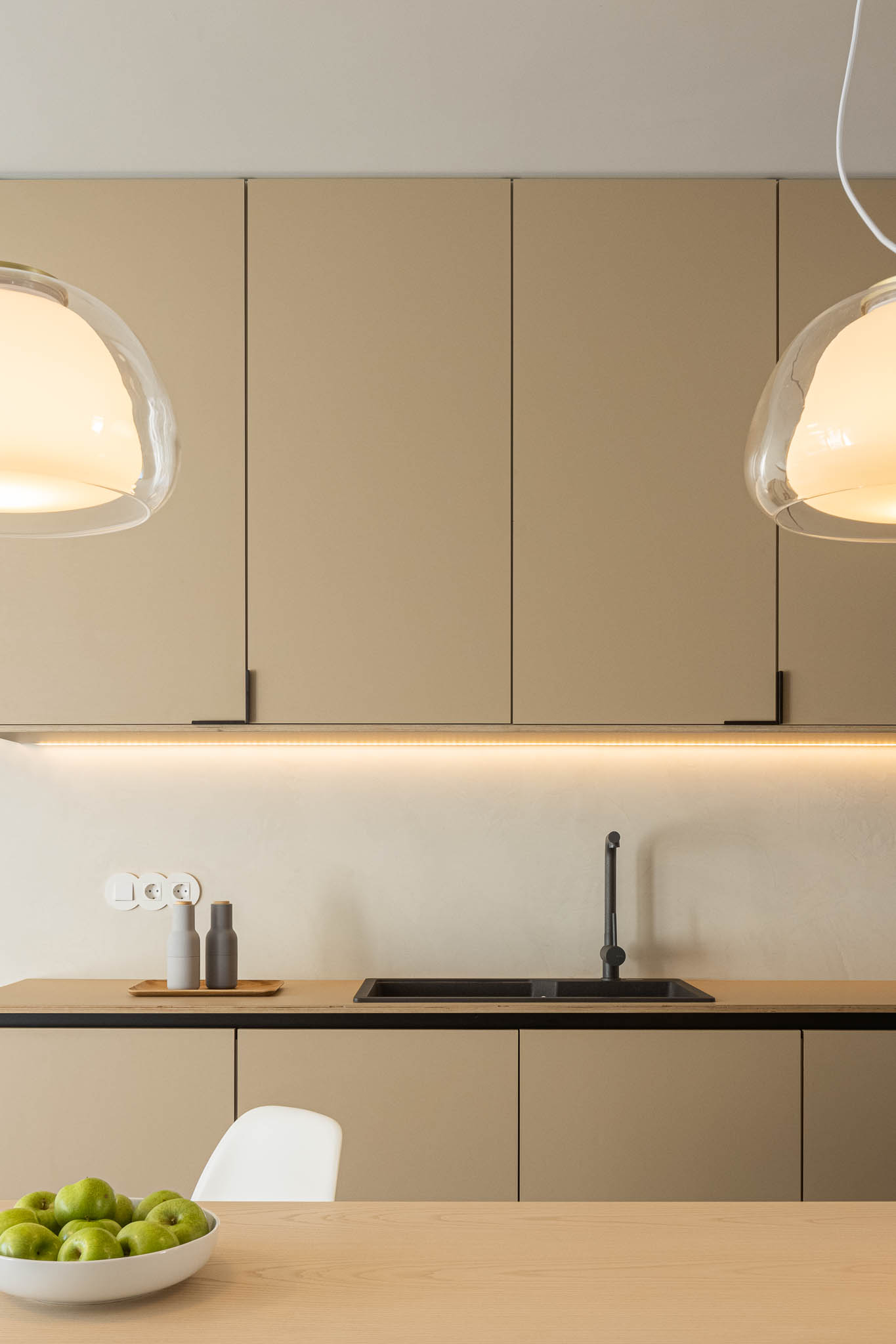 Detalhe da cozinha com armários bege, lava-loiça preta e iluminação LED. Candeeiros suspensos de vidro. — Casa moinho de vento arquitetura BOX arquitectos em Ponta Delgada