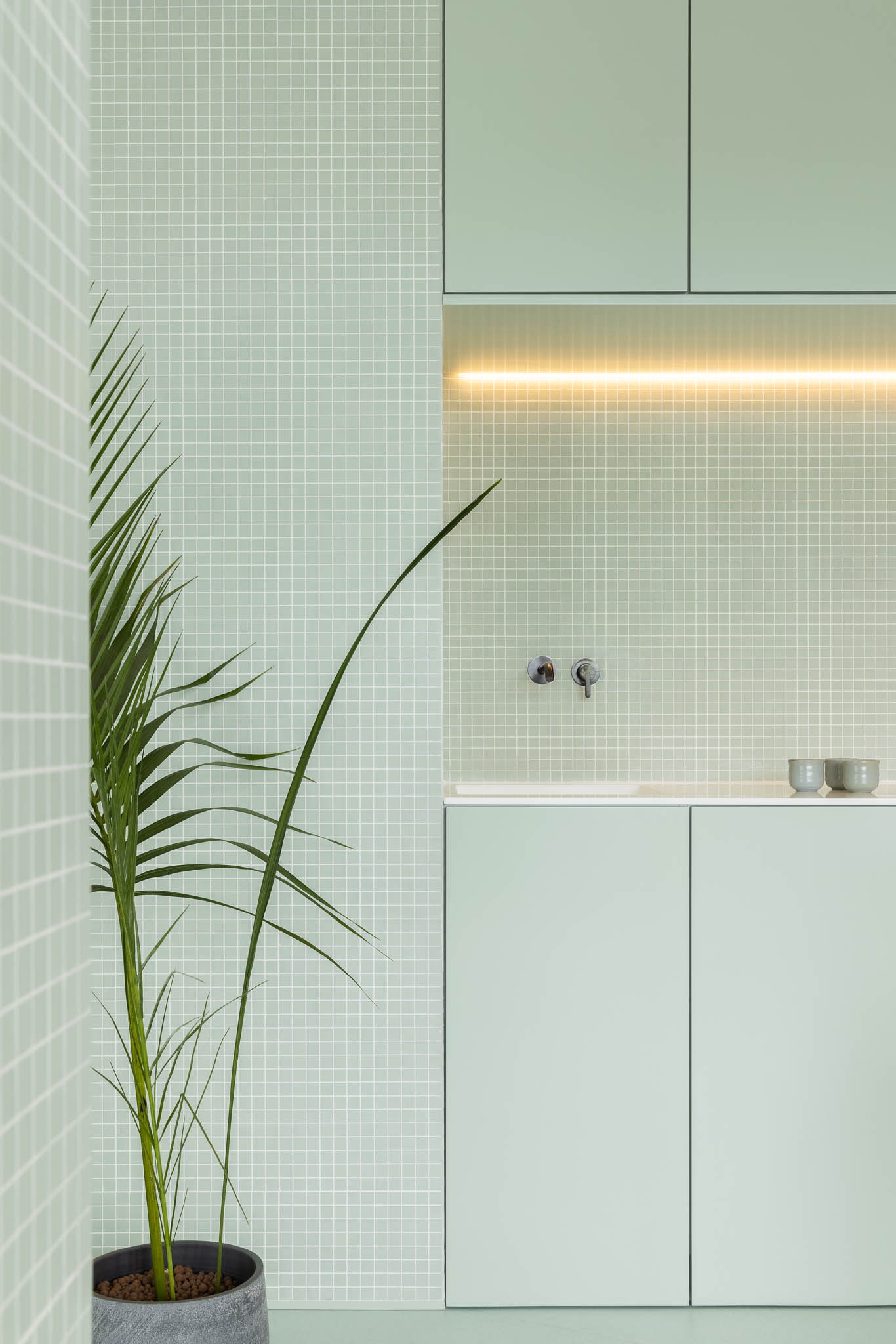 Lavabo com azulejos verde-água, armários minimalistas e iluminação linear, destacando a simplicidade e higiene do espaço. — Think Health Naturopatia arquitetura BOX arquitectos em Ponta Delgada