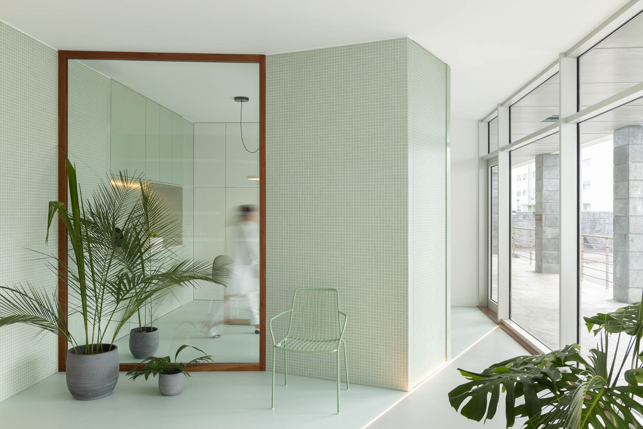 Sala de espera com espelho amplo, azulejos verde-água, cadeira metálica e plantas, promovendo um ambiente relaxante e natural. — Think Health Naturopatia arquitetura BOX arquitectos em Ponta Delgada