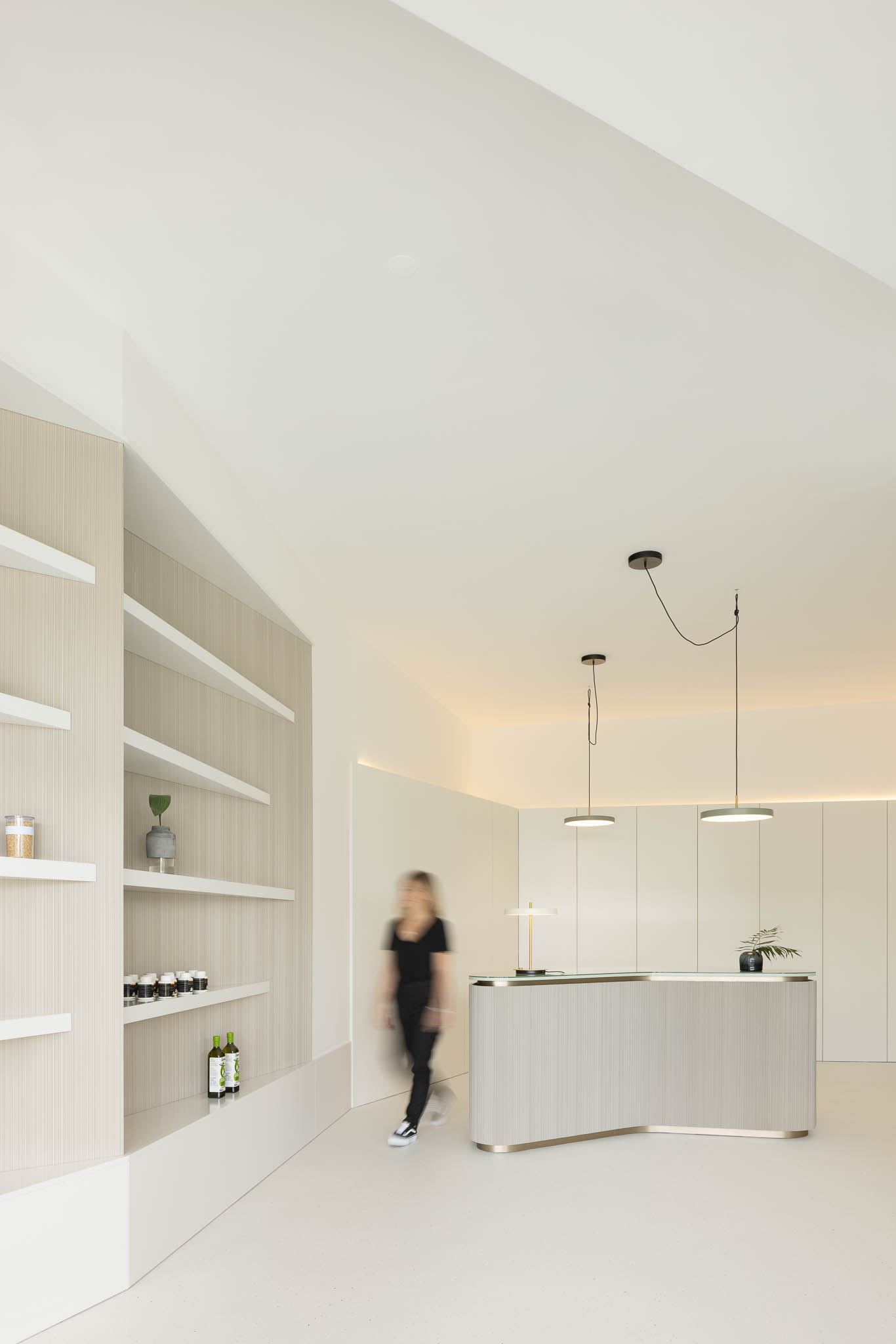 Recepção minimalista com balcão em madeira clara, prateleiras embutidas e iluminação suave, transmitindo uma sensação de serenidade. — Think Health Naturopatia arquitetura BOX arquitectos em Ponta Delgada
