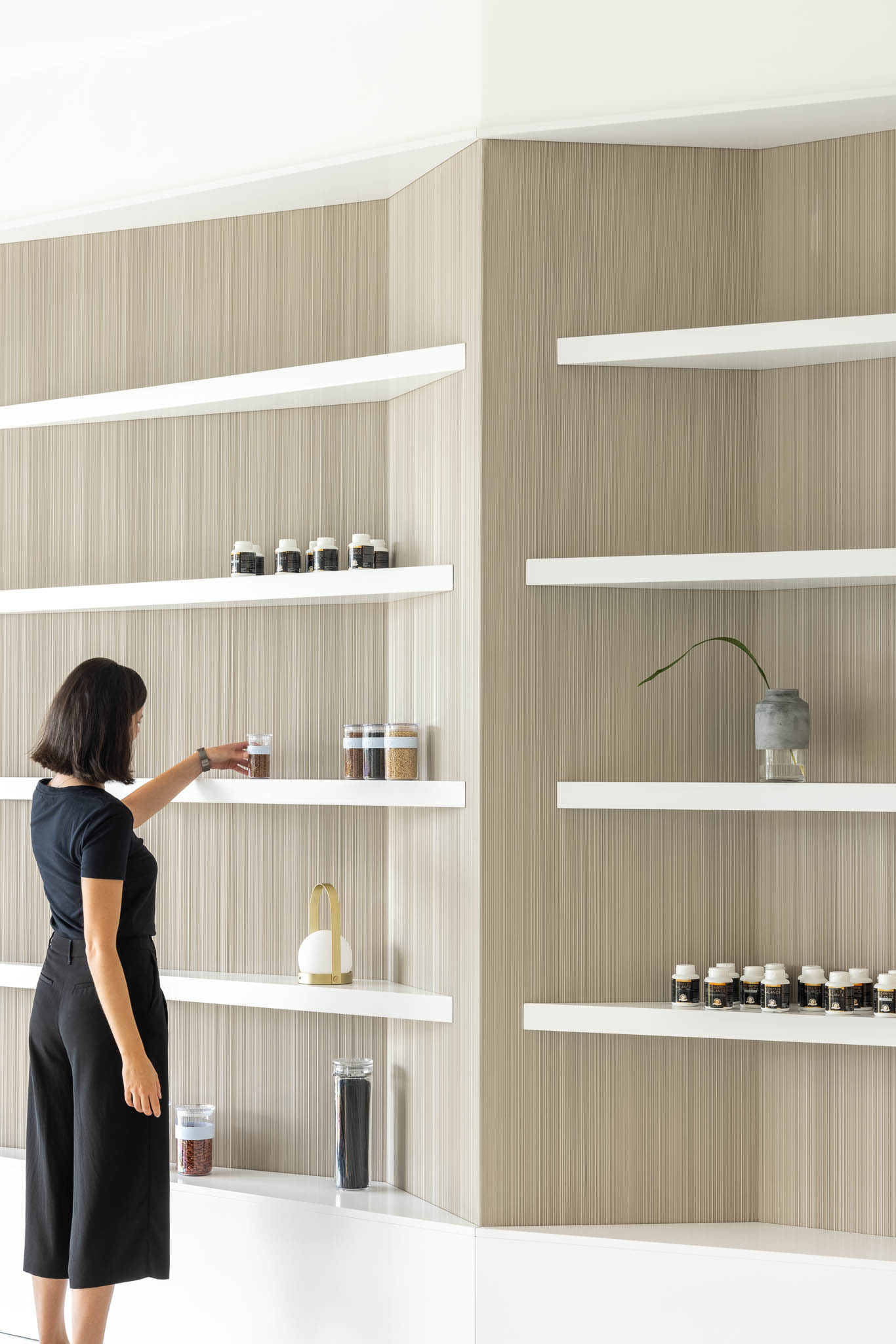 Estante com prateleiras brancas e fundo em madeira clara, exibindo produtos naturais e decorativos, enfatizando a oferta da naturopatia. — Think Health Naturopatia arquitetura BOX arquitectos em Ponta Delgada