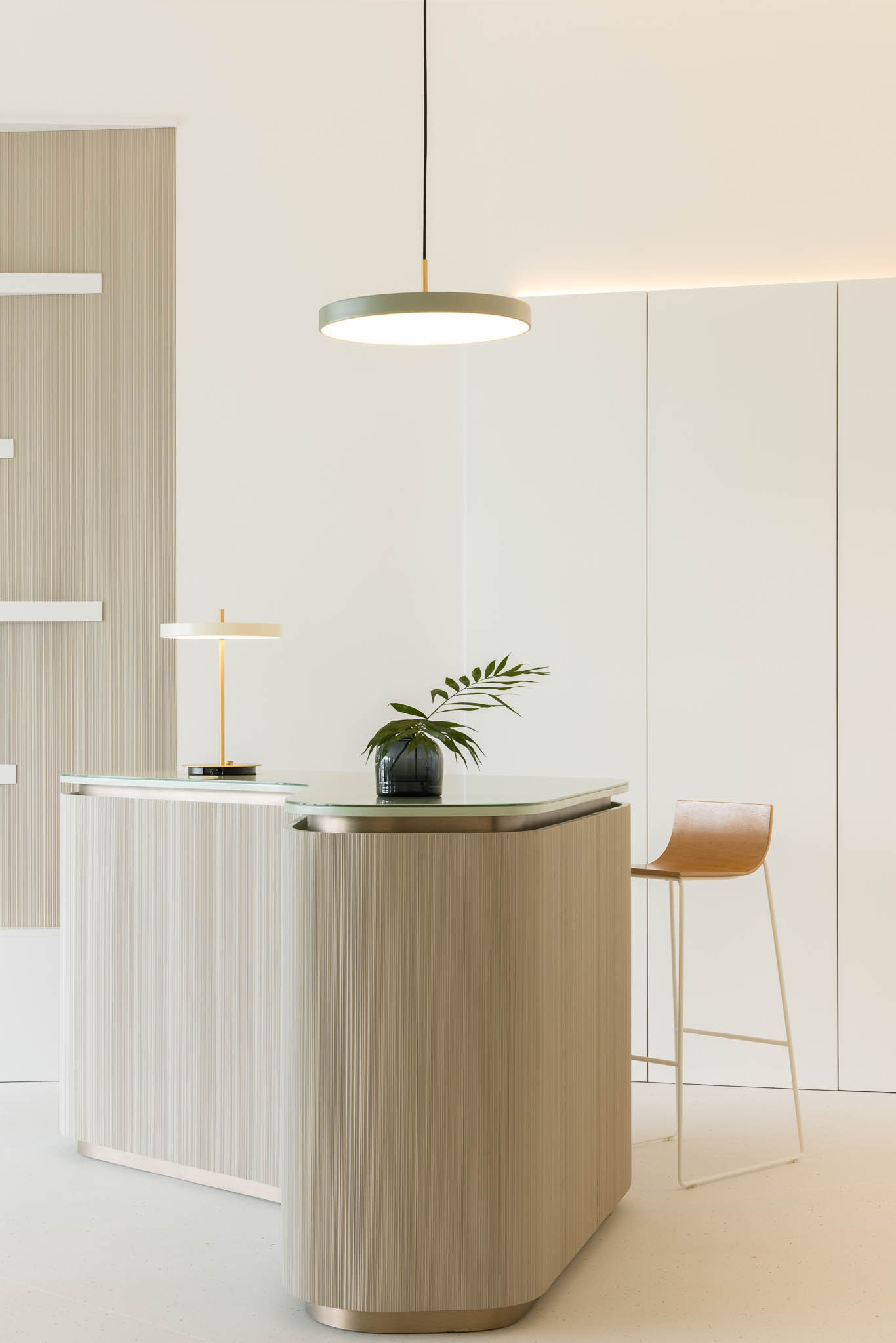 Detalhe do balcão de receção com iluminação pendente, cadeira alta e decoração minimalista, criando um espaço acolhedor e funcional. — Think Health Naturopatia arquitetura BOX arquitectos em Ponta Delgada