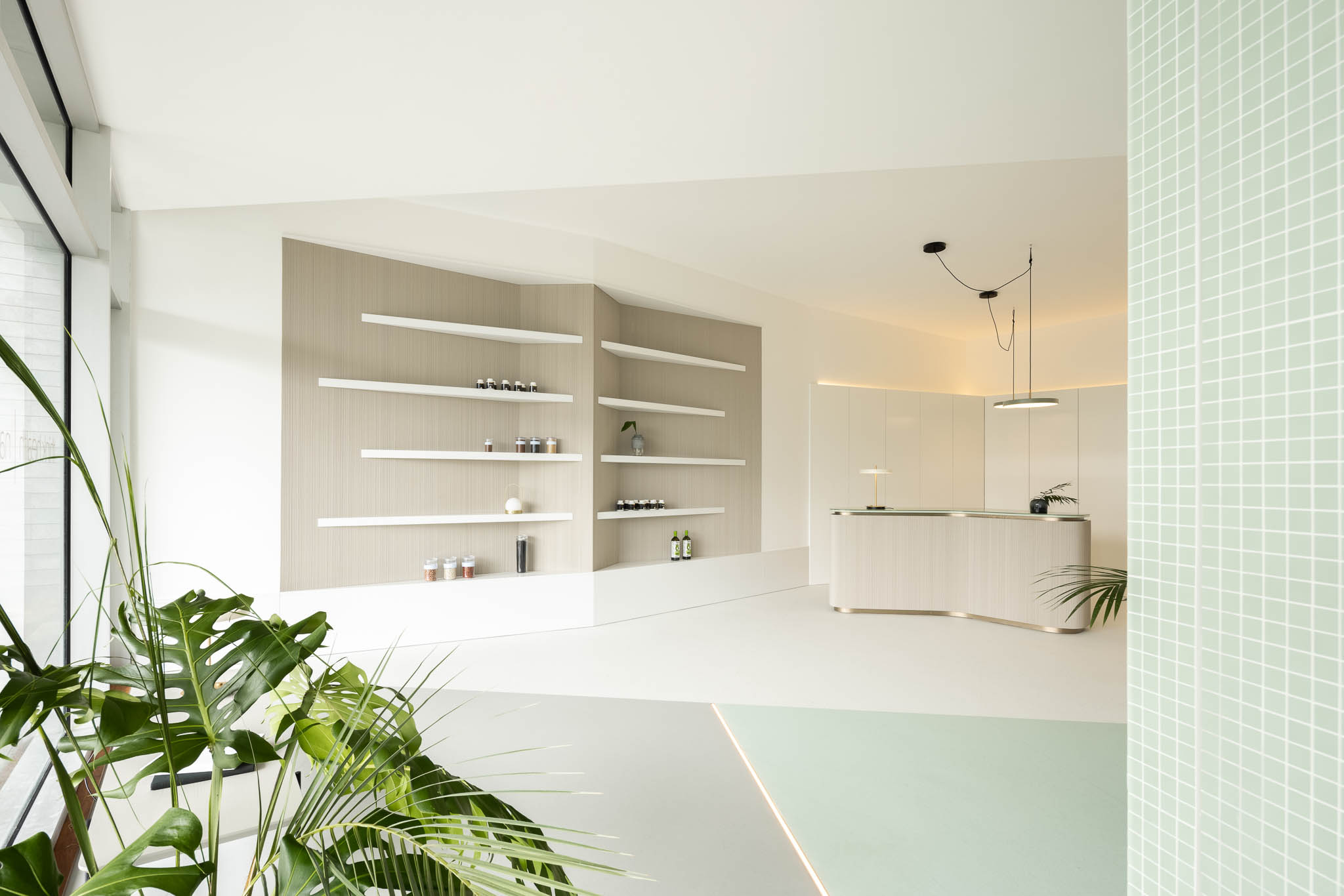 Espaço amplo com estante, balcão de receção e divisórias em azulejo verde-água, integrando diferentes áreas de forma harmoniosa. — Think Health Naturopatia arquitetura BOX arquitectos em Ponta Delgada