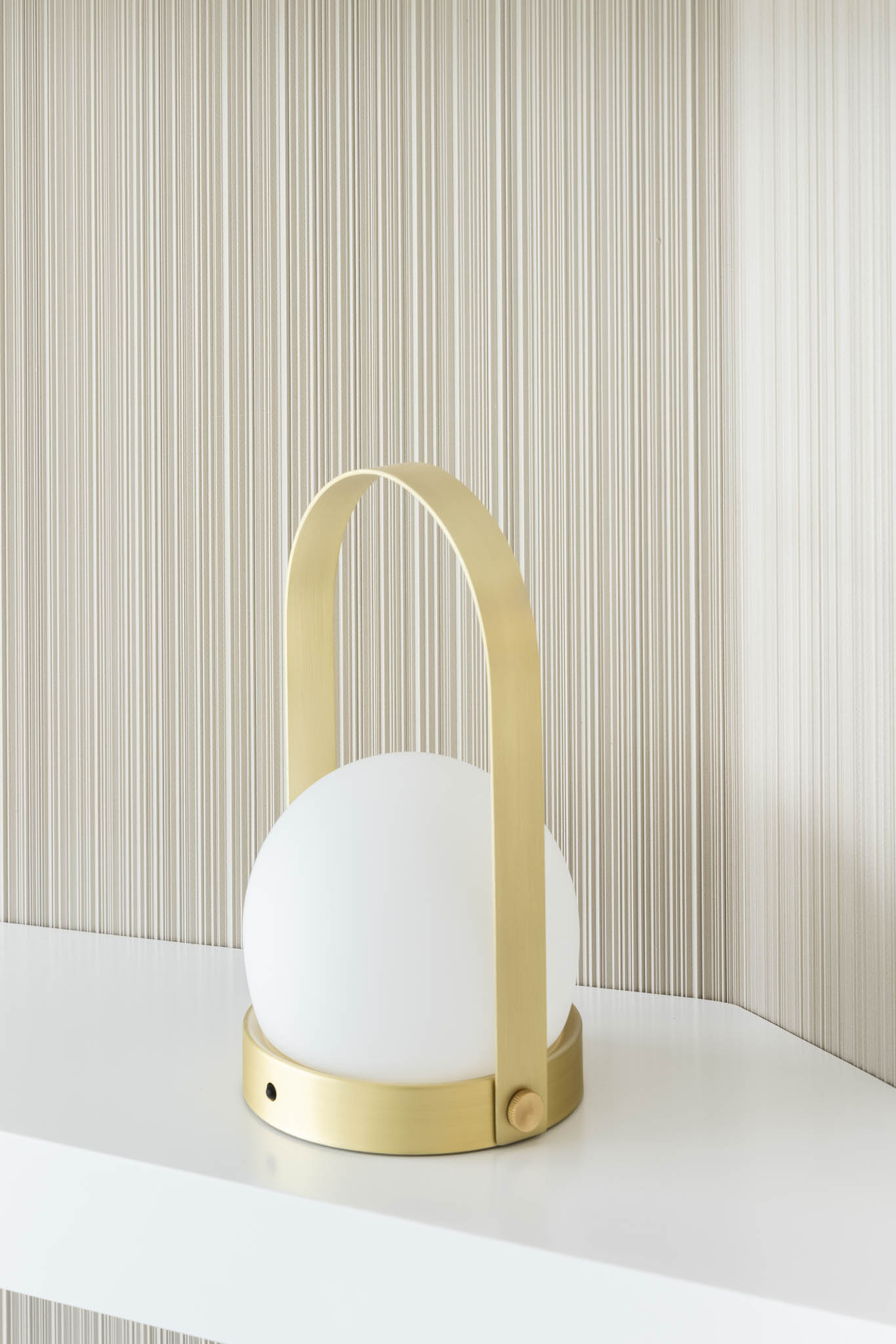 Candeeiro portátil com base dourada e globo branco sobre uma prateleira, combinando funcionalidade e estética minimalista. — Think Health Naturopatia arquitetura BOX arquitectos em Ponta Delgada