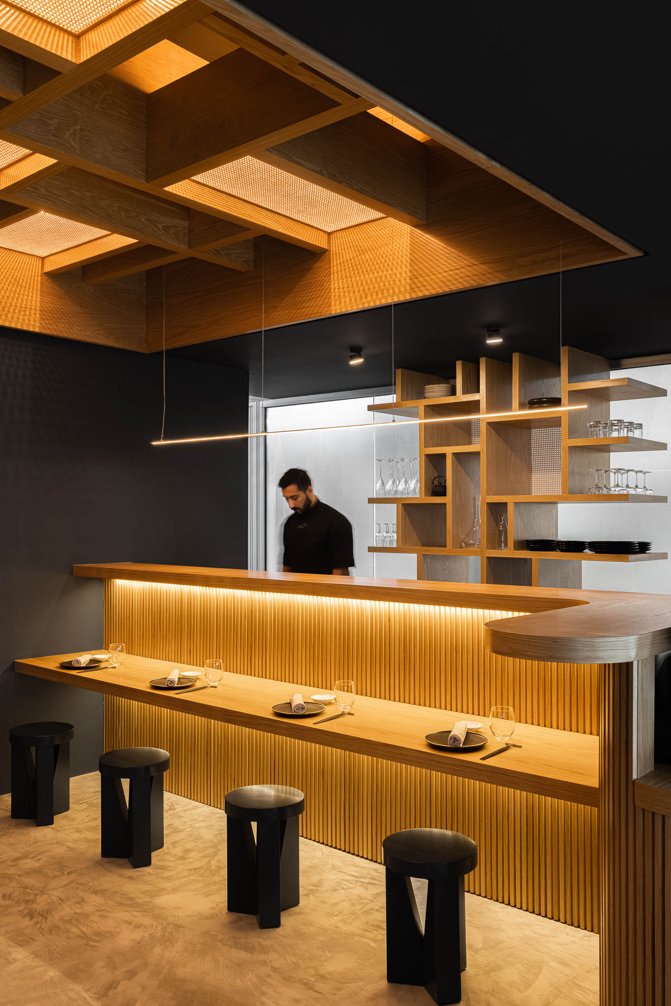 Interior do restaurante com balcão iluminado, cadeiras pretas e um funcionário, destacando a estética japonesa moderna. — Restaurante Fuji arquitetura Sequeira Dias Arquitectos em Ponta Delgada
