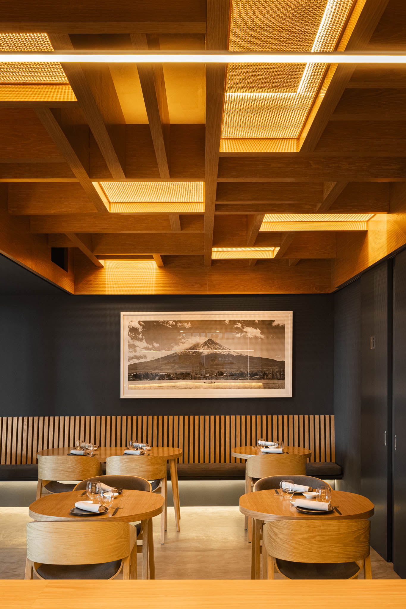 Sala de jantar com mesas e cadeiras em madeira clara, teto em madeira com iluminação e um quadro da montanha Fuji. — Restaurante Fuji arquitetura Sequeira Dias Arquitectos em Ponta Delgada