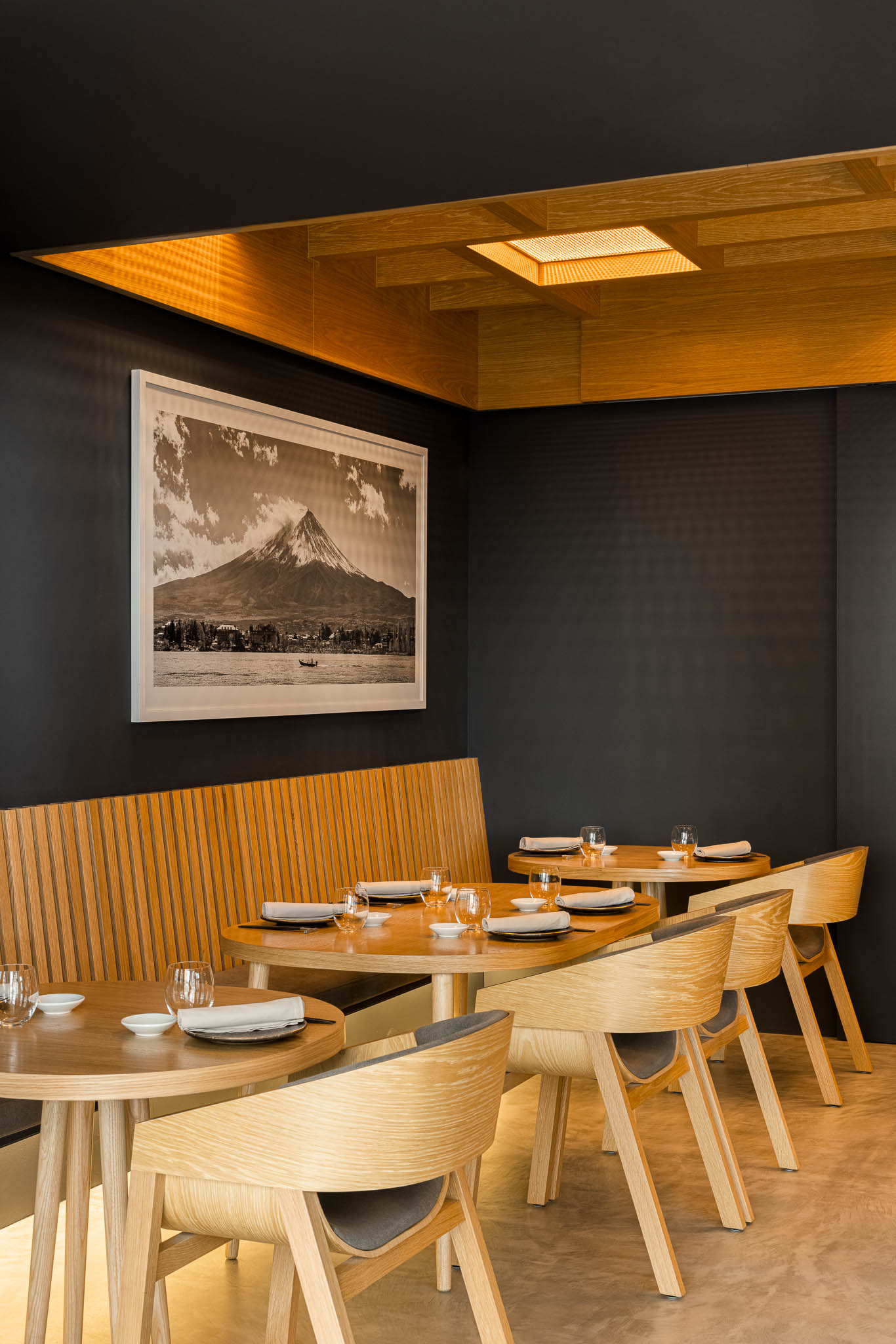 Espaço de refeições com sofás e cadeiras em madeira clara, quadro da montanha Fuji e iluminação ambiente. — Restaurante Fuji arquitetura Sequeira Dias Arquitectos em Ponta Delgada