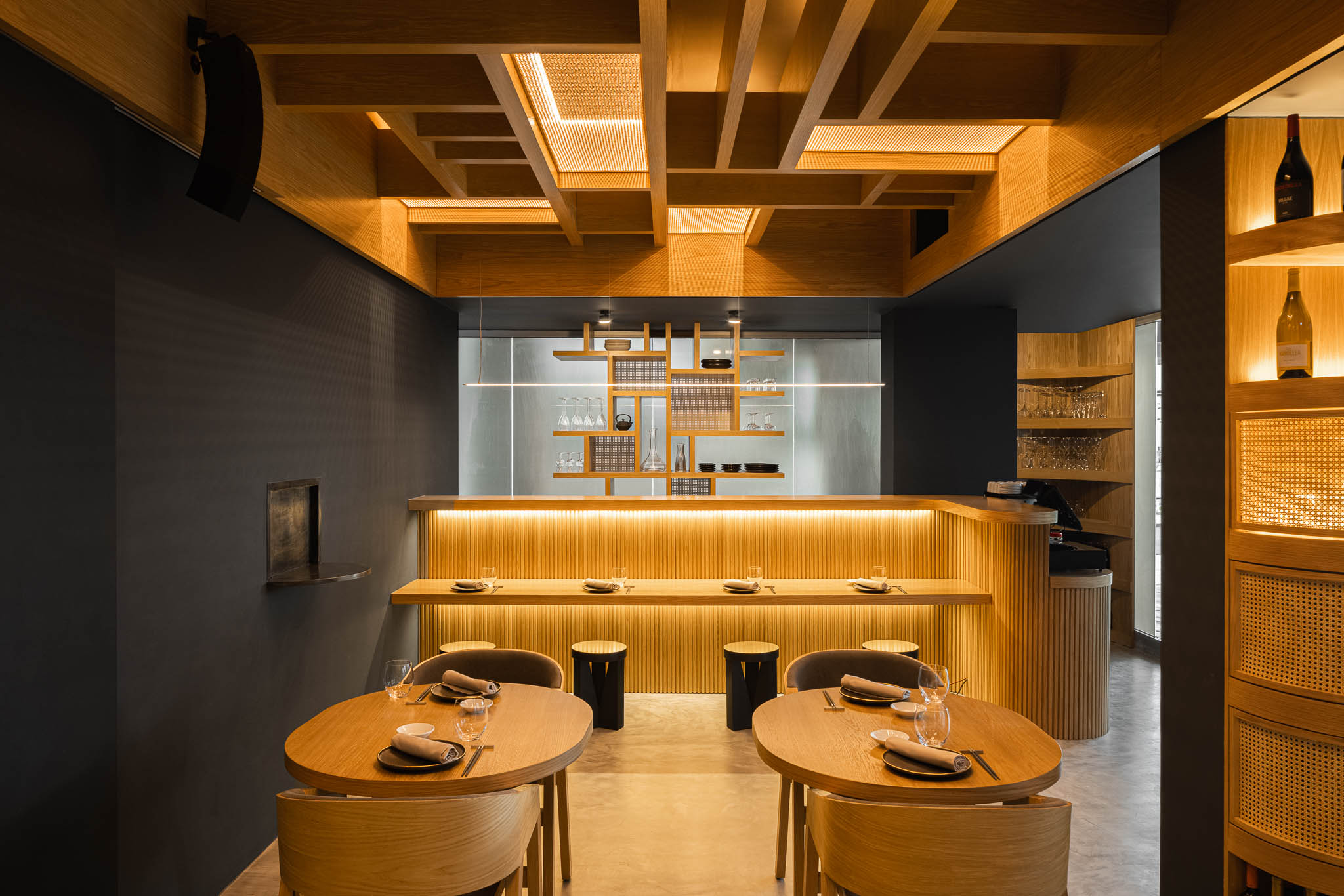 Vista geral do restaurante com balcão, mesas e cadeiras em madeira, destacando o design minimalista e a iluminação. — Restaurante Fuji arquitetura Sequeira Dias Arquitectos em Ponta Delgada